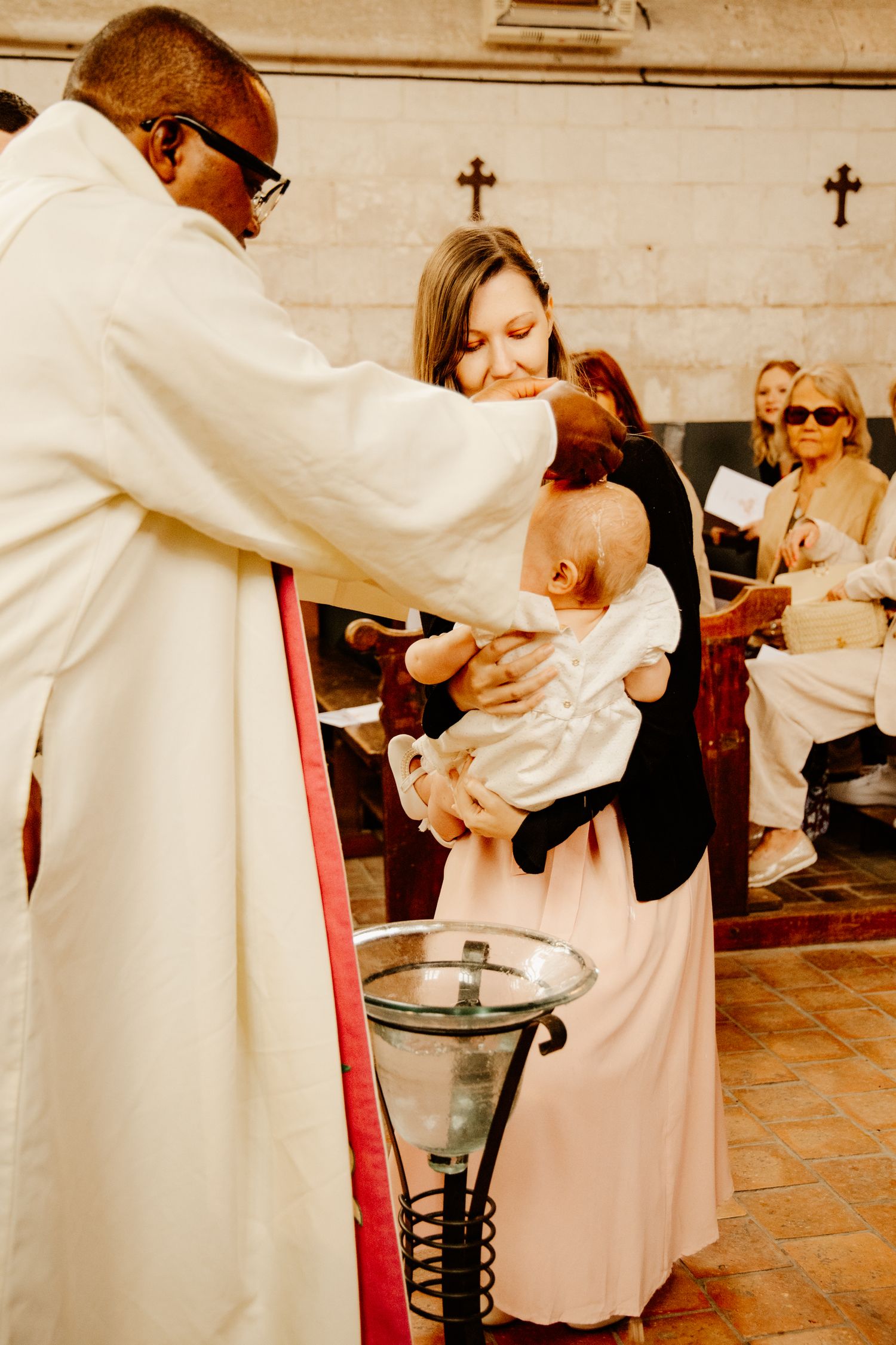 prêtre qui baptise un bébé dans les bras de sa tante