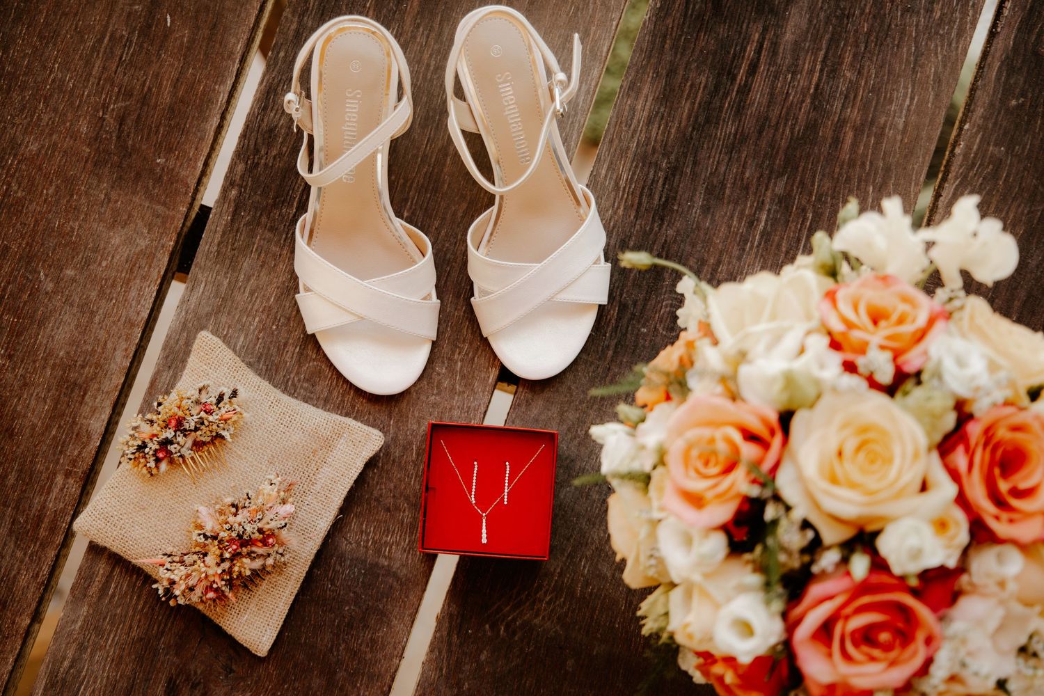 À plat des accessoires du mariage : chaussures de la mariée, alliances dans leur écrin et bouquet de fleurs.