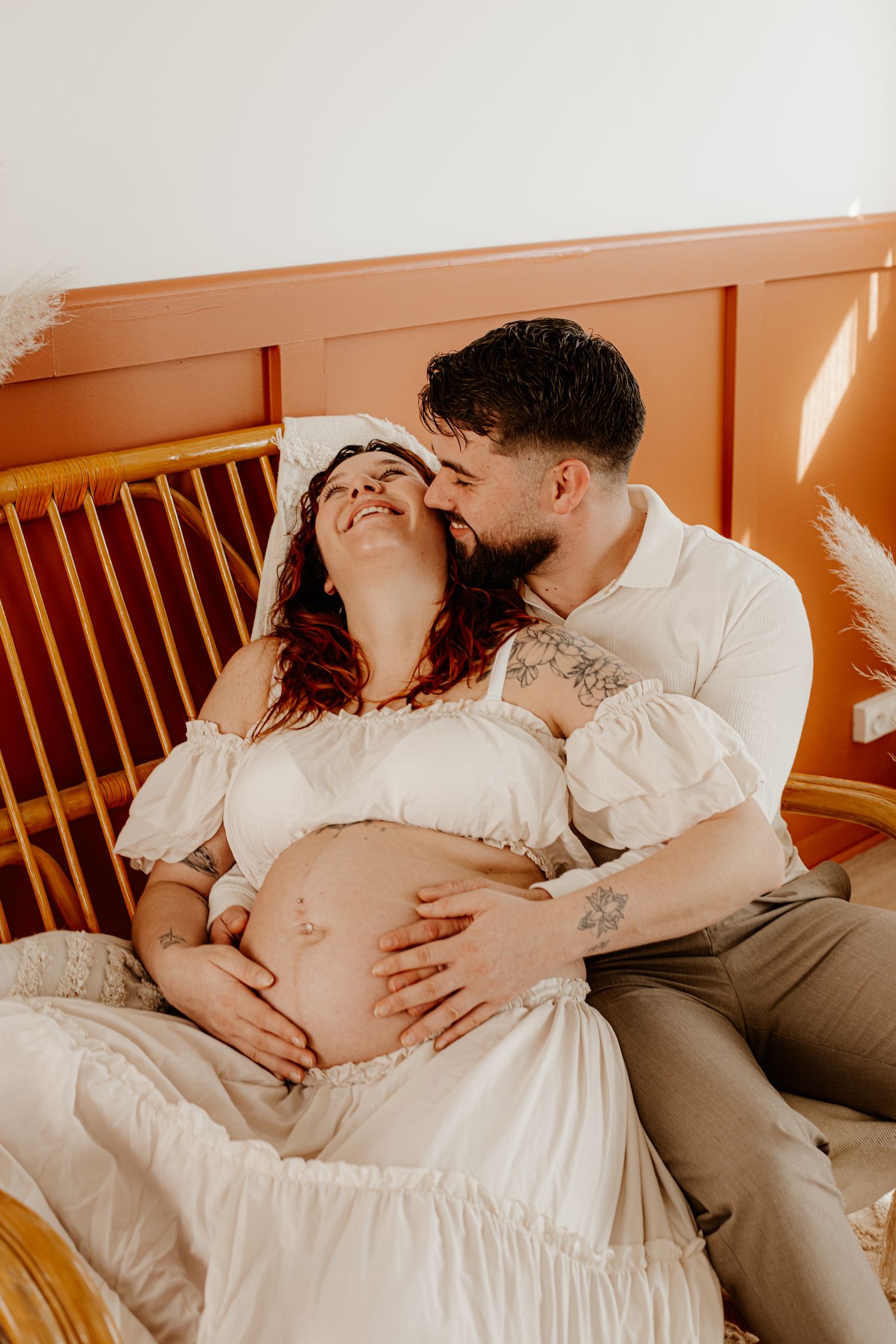 Rires et complicité d'un jeune couple pendant leur séance photo grossesse en studio. Photographe maternité.