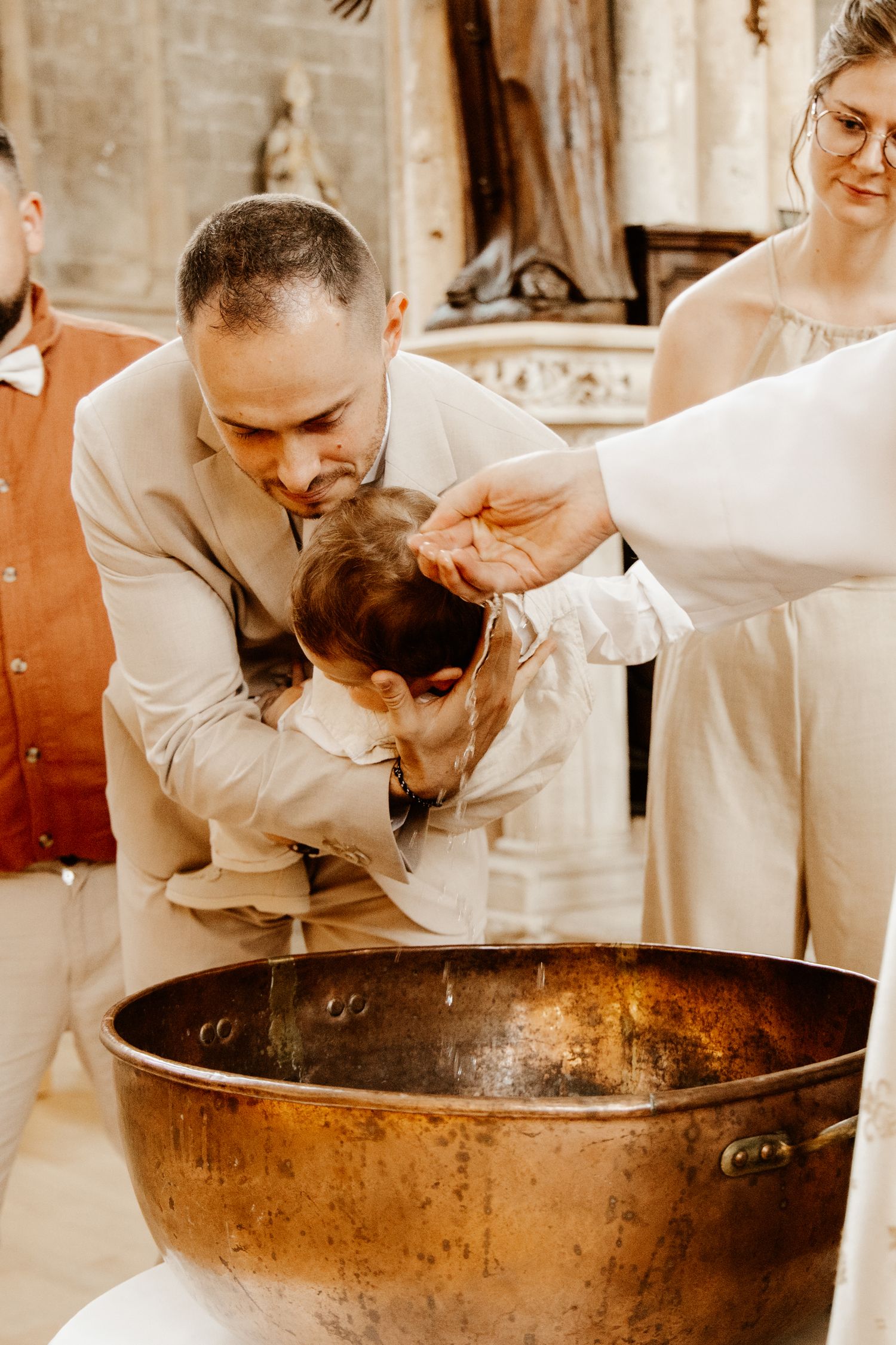 papa qui tien dans les mains son fils qui se fait baptiser par le prêtre lors de son baptême