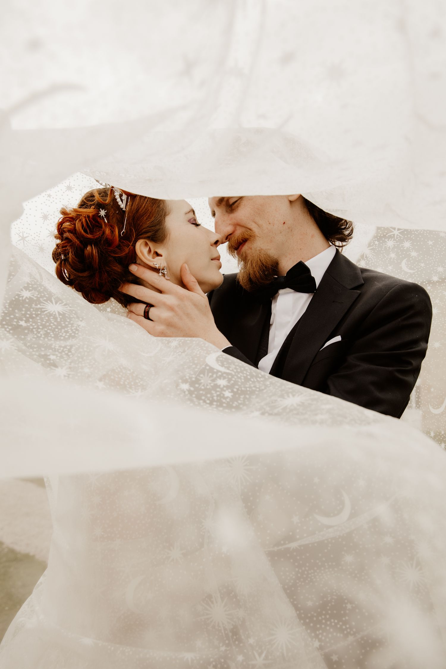 Portrait intimiste de mariés se regardant dans les yeux sous le voile. Séance photo de couple par photographe.