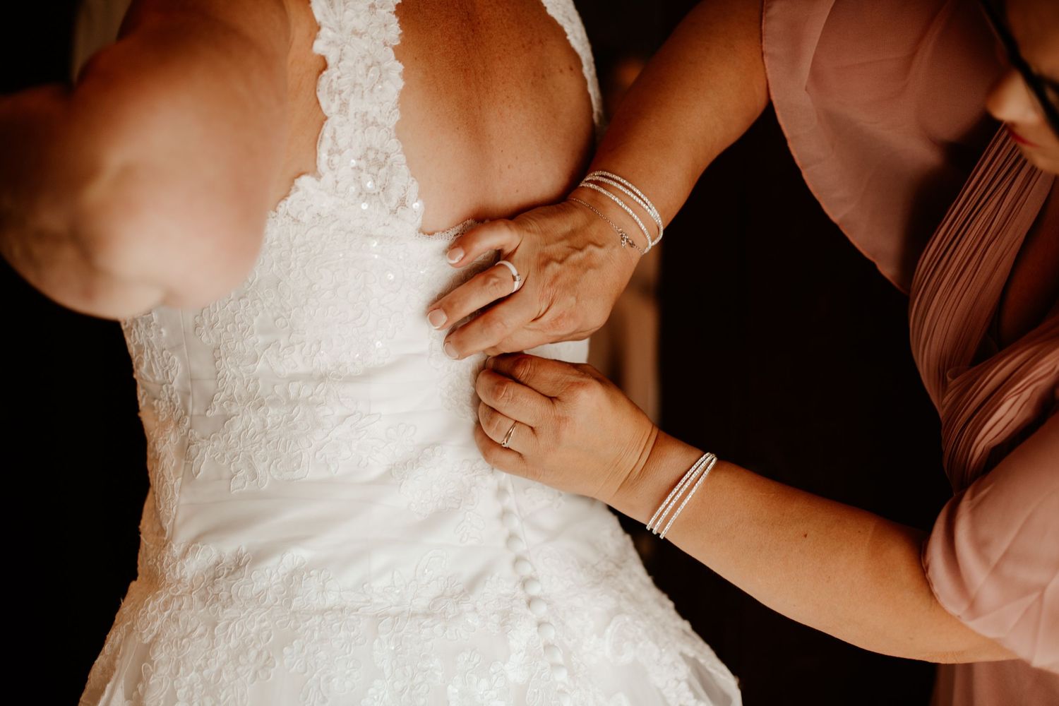 La témoin de mariage aide à fermer et ajuster le dos de la robe de mariée en dentelle pendant les préparatifs.