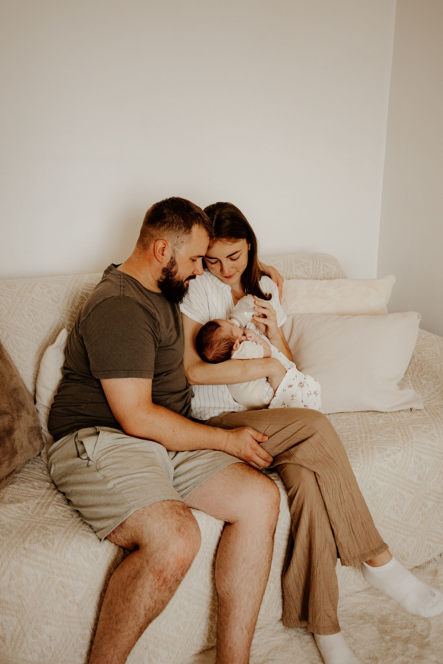 Jeunes parents donnant le biberon à leur nouveau-né lors d'une séance photo naissance au studio bohème d'Isaure Joly Photographie à Hédouvil