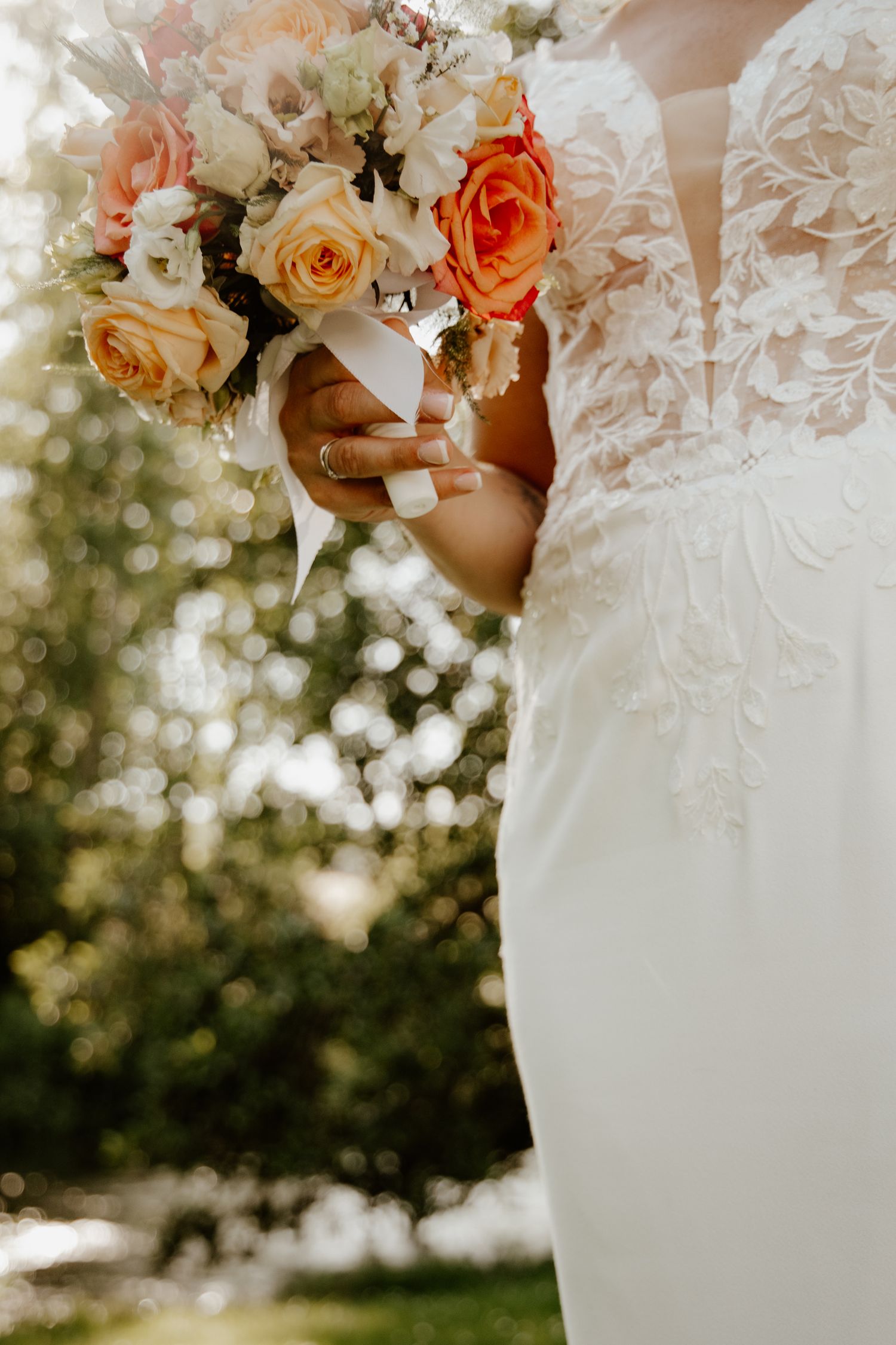 Bouquet de la mariée aux tons pastel tenu contre sa robe en dentelle fine.