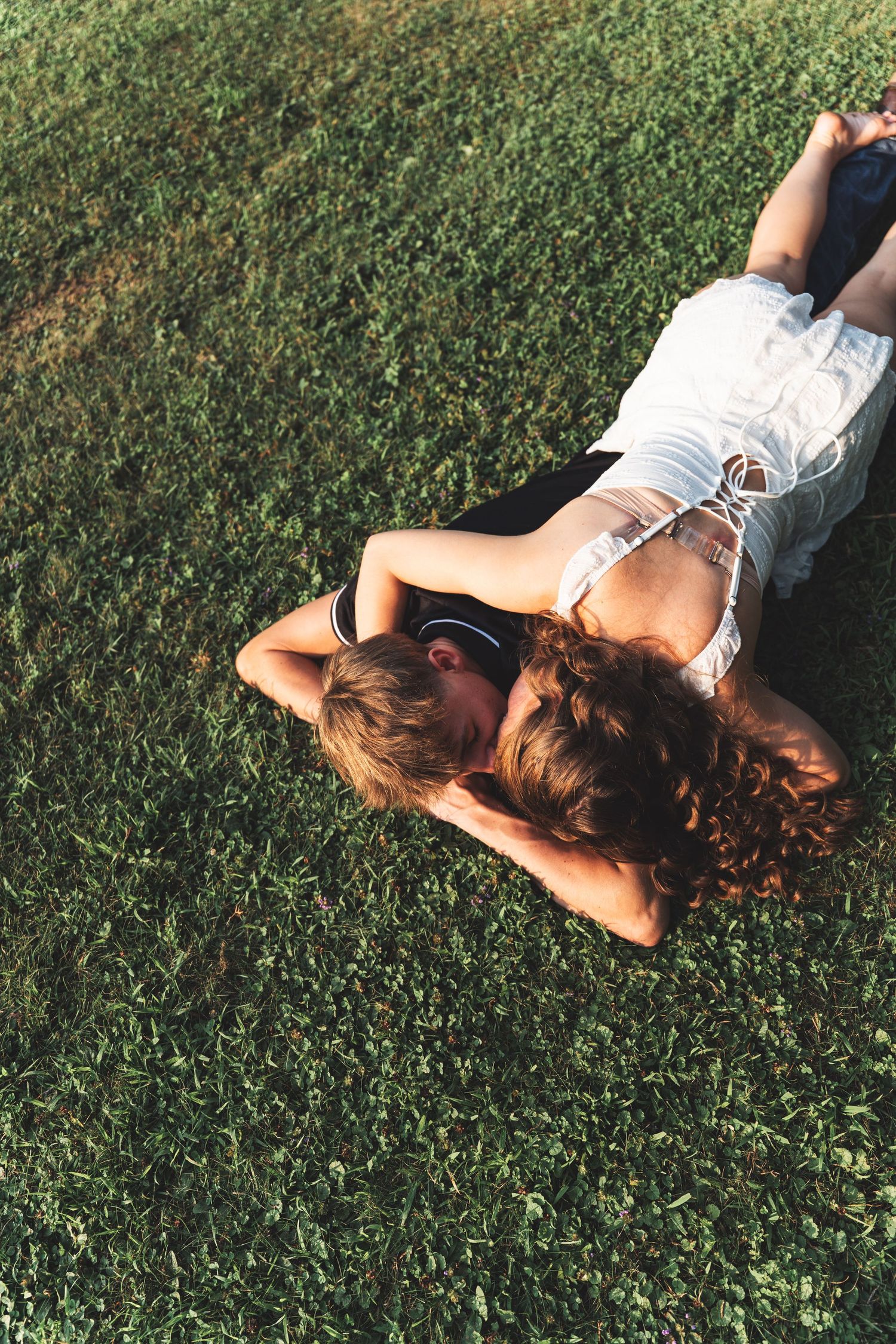 Couple lying together on lush green grass, viewed from above, enjoying a sunny day outdoors.