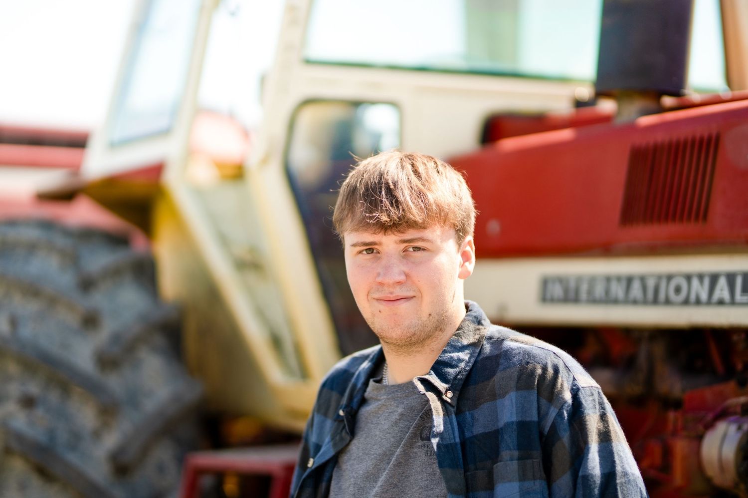 Young man in plaid shirt standing in front of a red International tractor outdoors.