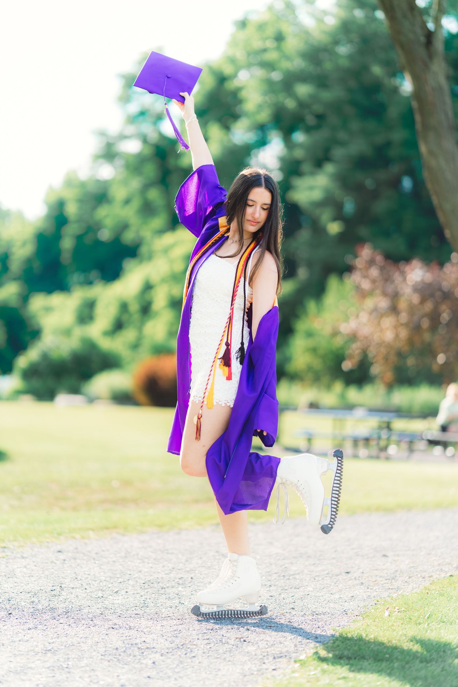 Graduate in purple gown celebrating outdoors, raising cap in the air joyfully.