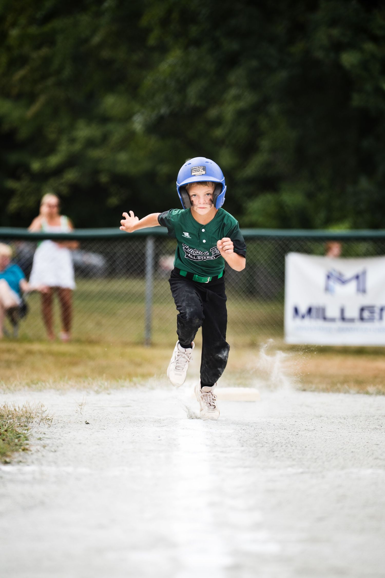 Young baseball player in green jersey and blue helmet running bases during a youth league game.