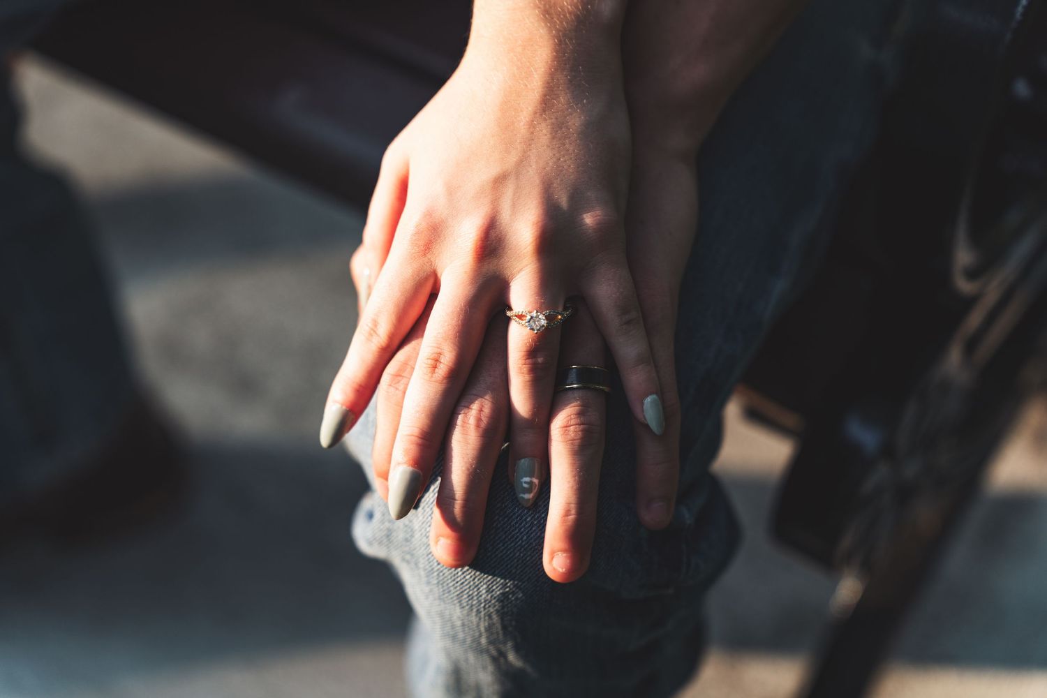 Two hands gently resting together on denim jeans, one adorned with delicate stacked rings, in warm natural light.