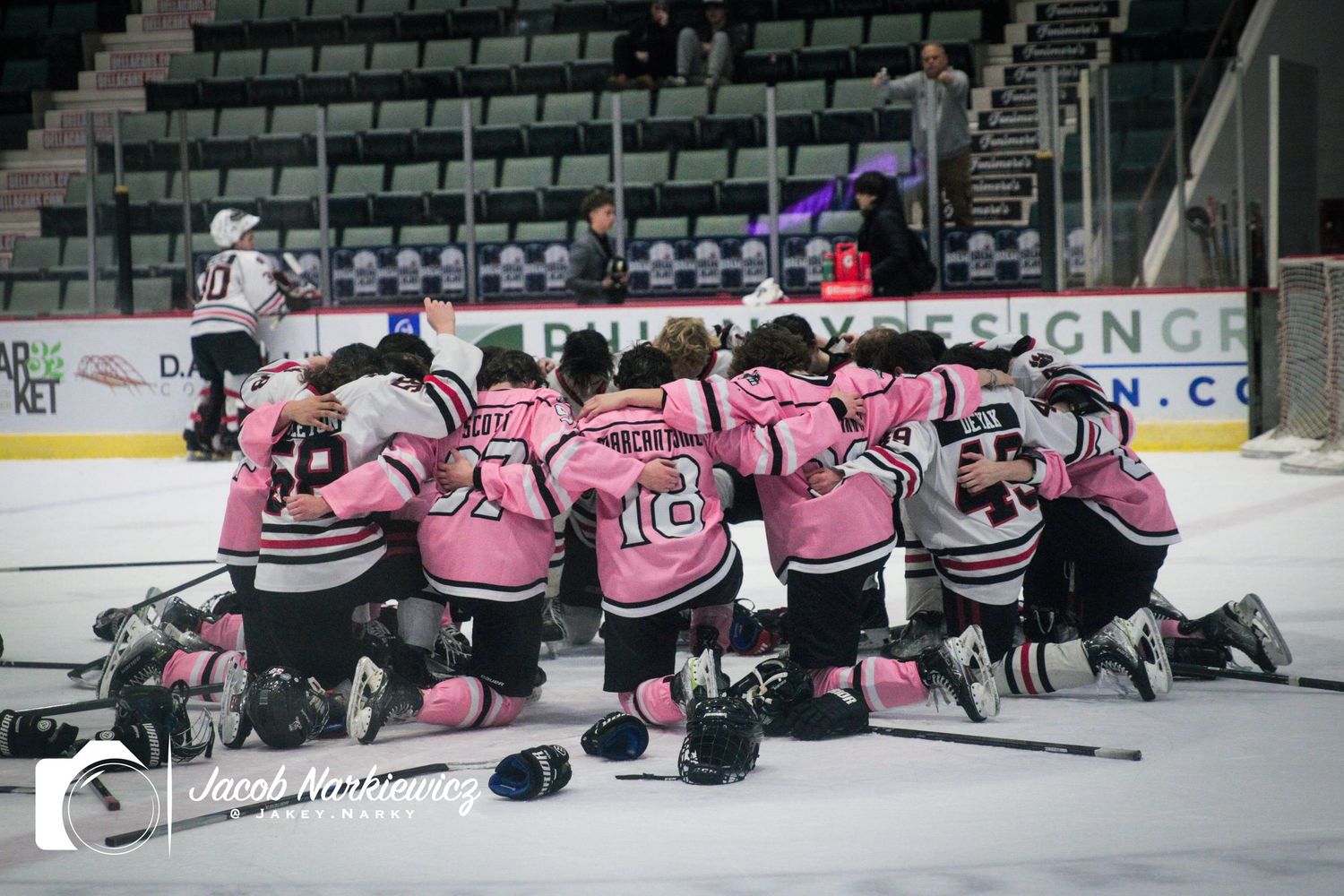 Youth hockey team in pink jerseys huddle together on ice rink after game.