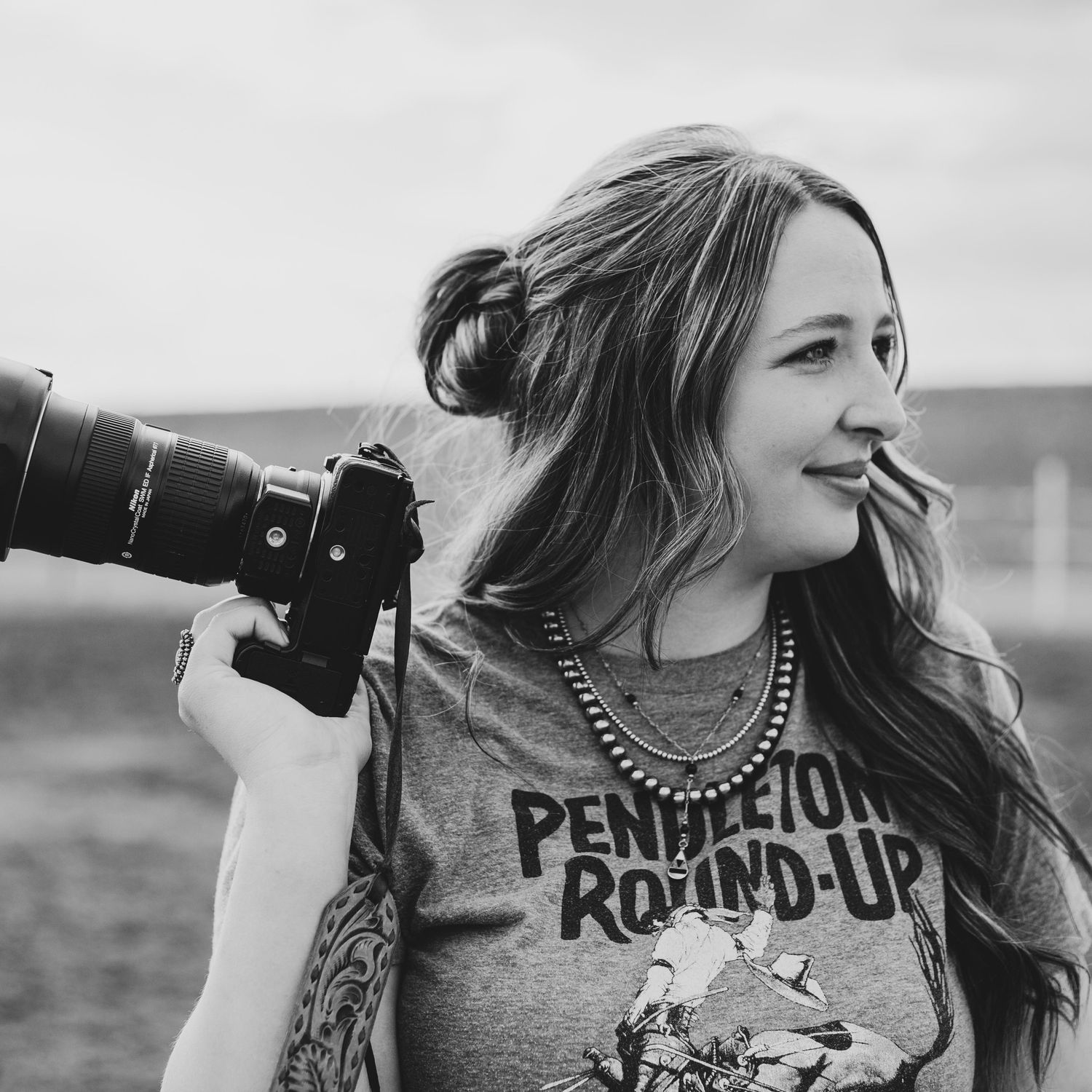 Woman holding a DSLR camera wearing a Pendleton Round-Up shirt in a black and white outdoor portrait.