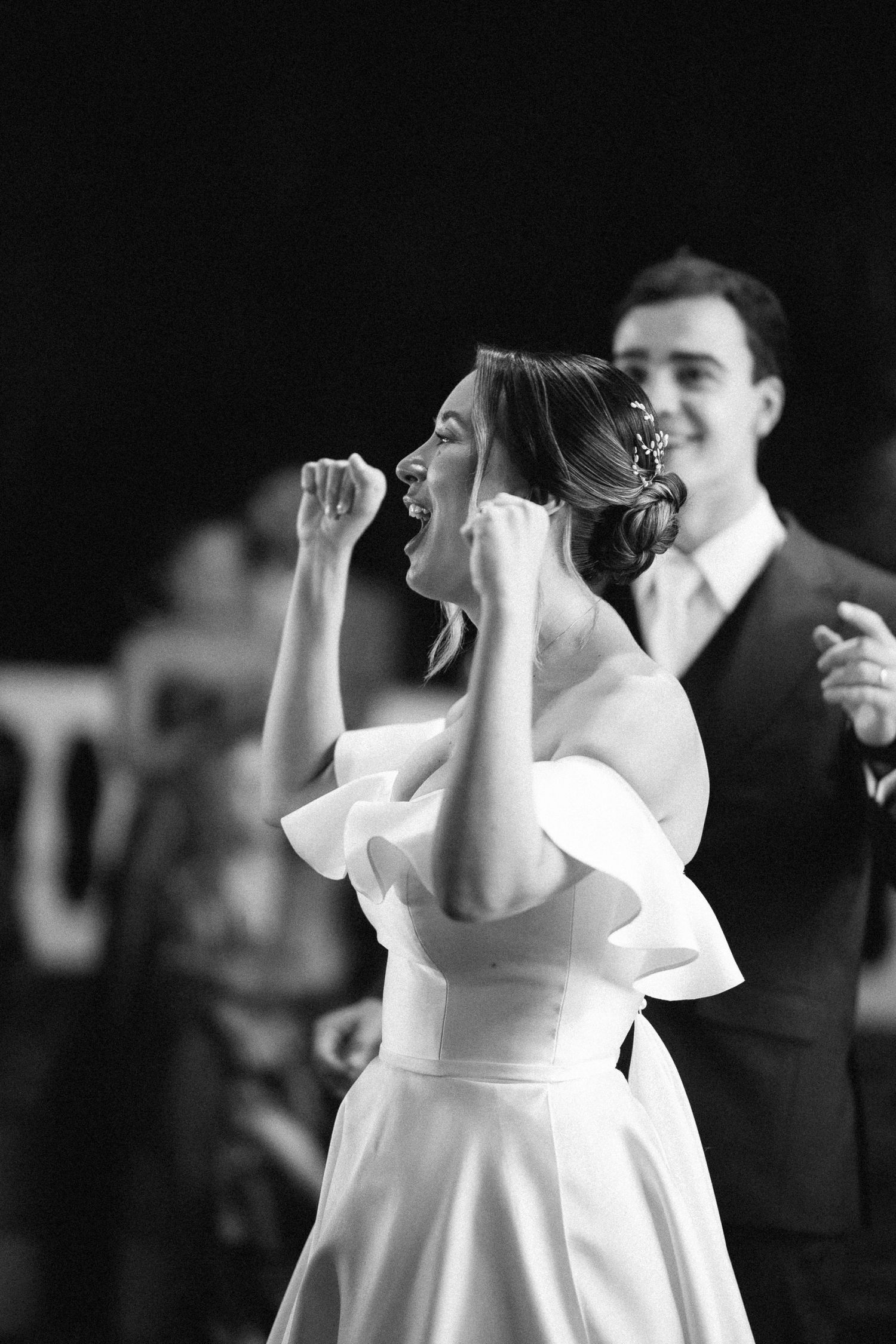 Black and white photo of an excited bride pumping her fists while dancing with her groom at their wedding reception.