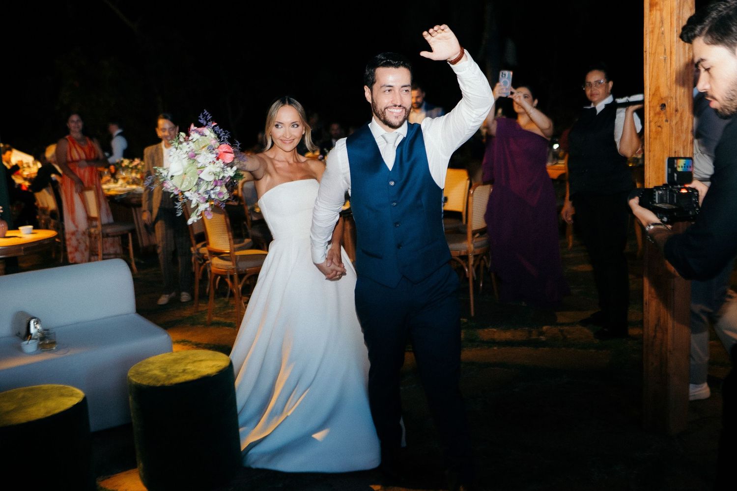 Bride and groom make grand reception entrance as groom raises arm triumphantly in elegant evening wedding celebration.