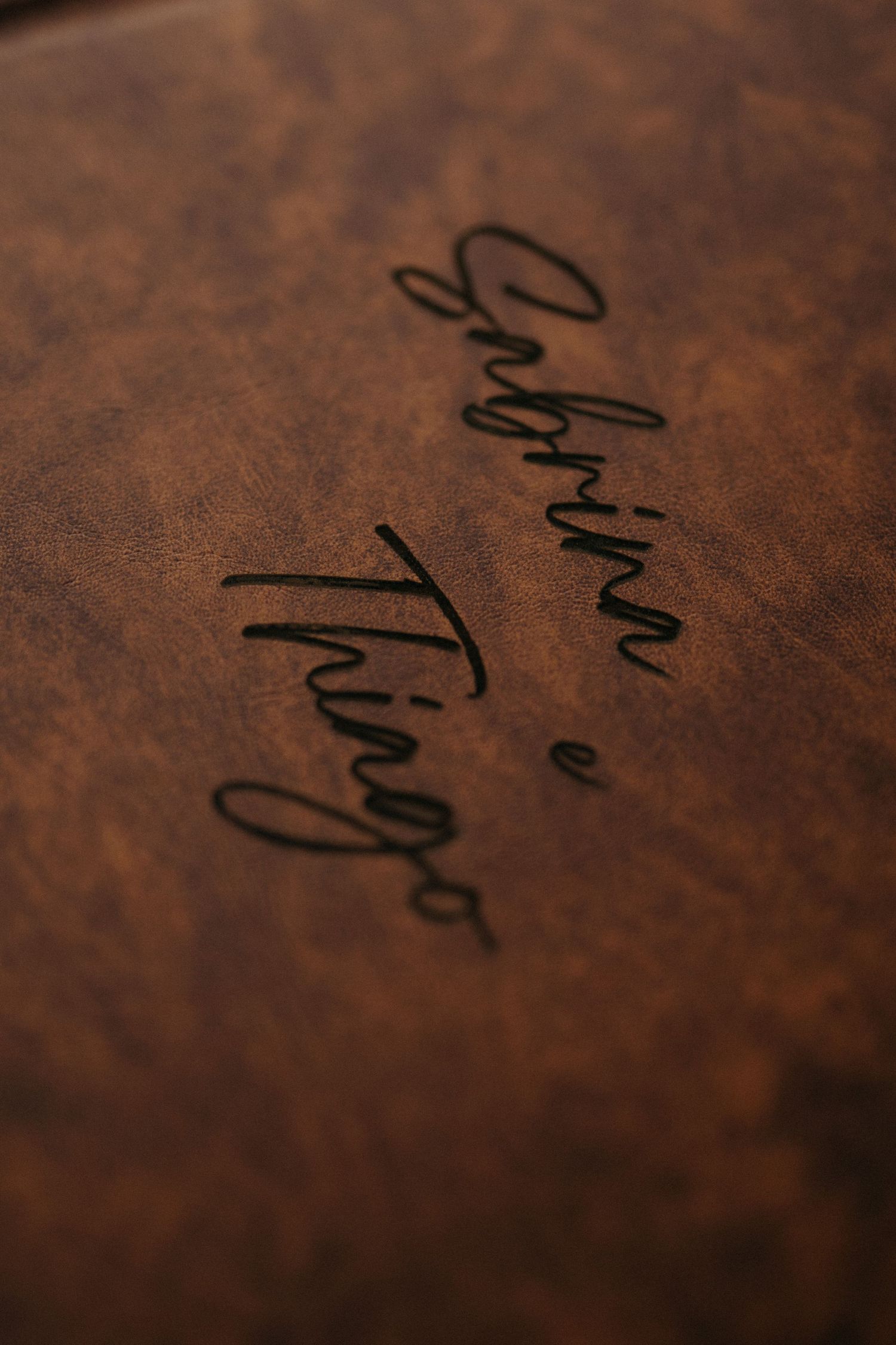 Close-up of brown leather book embossed with elegant cursive script reading Gabriina e Tiago.