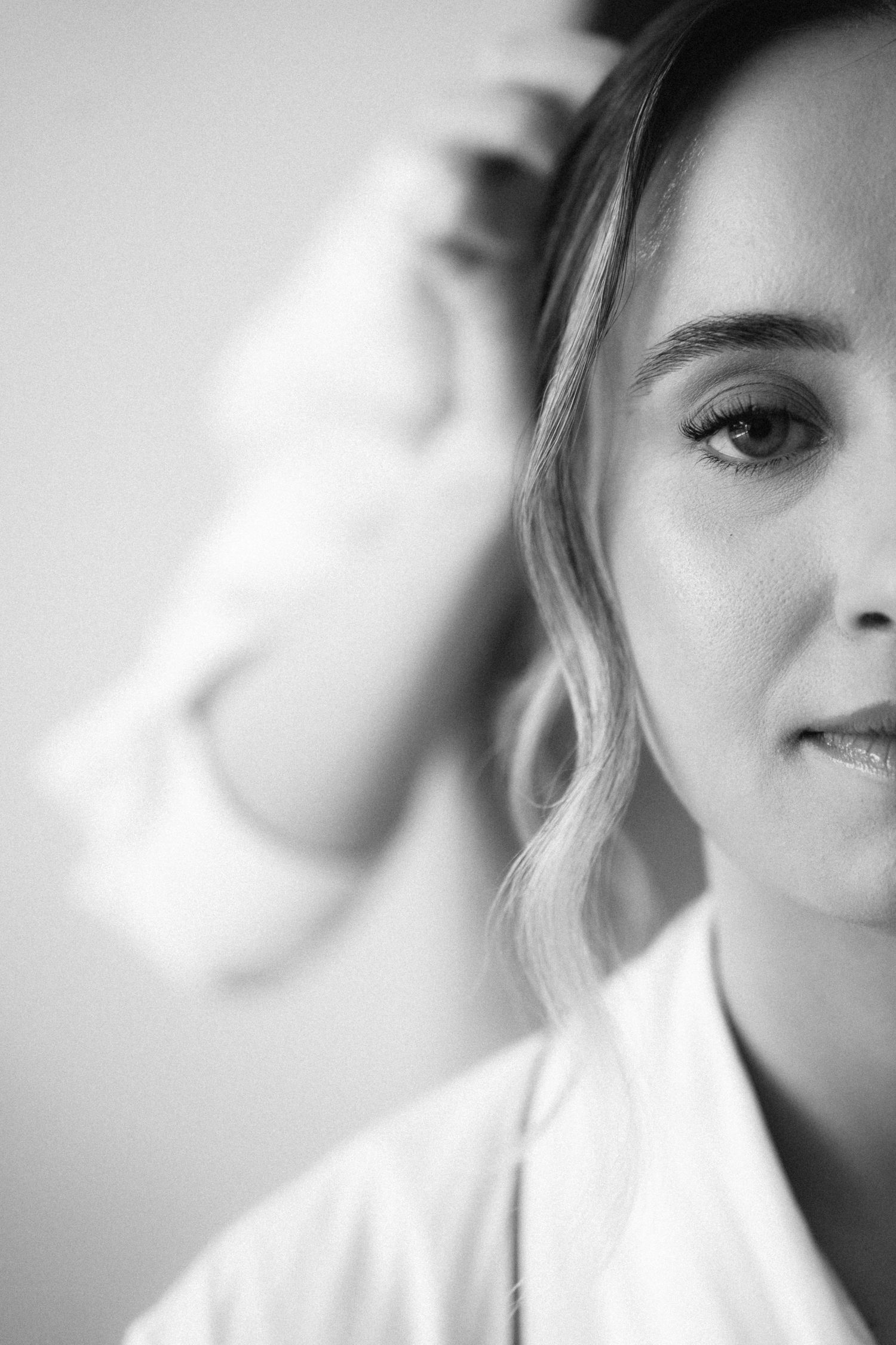 Black and white close-up portrait of a young woman touching her hair in soft light.
