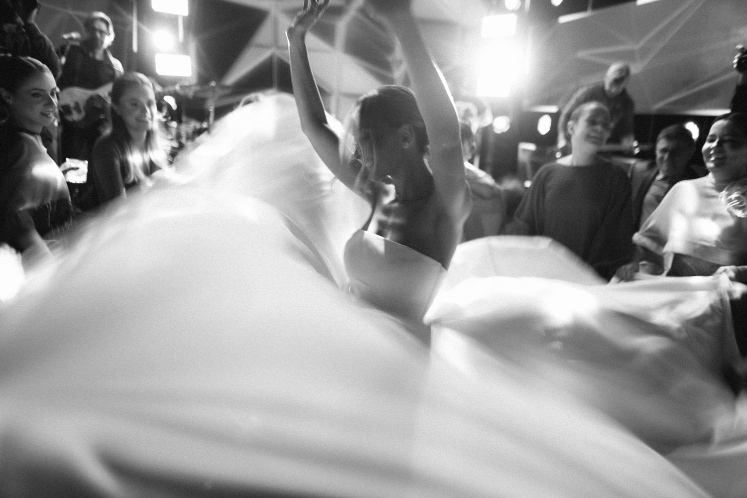 Black and white photo of bride dancing joyfully with guests at wedding reception.