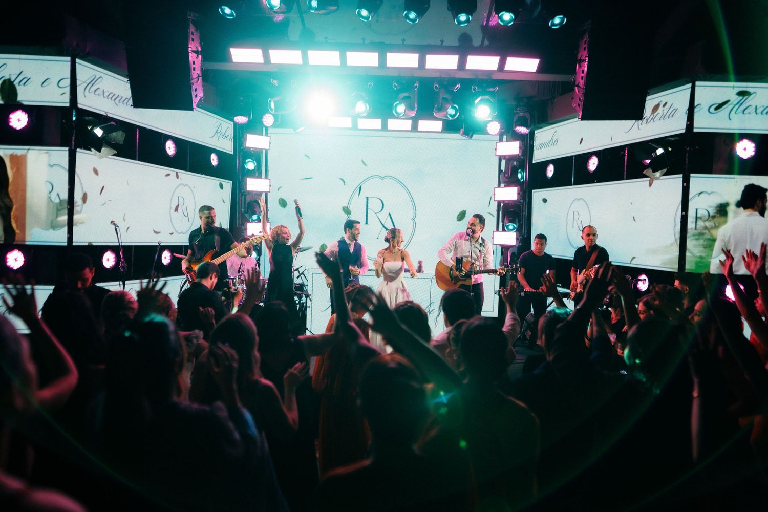 Live band performs on a bright stage surrounded by LED screens at an elegant wedding reception.