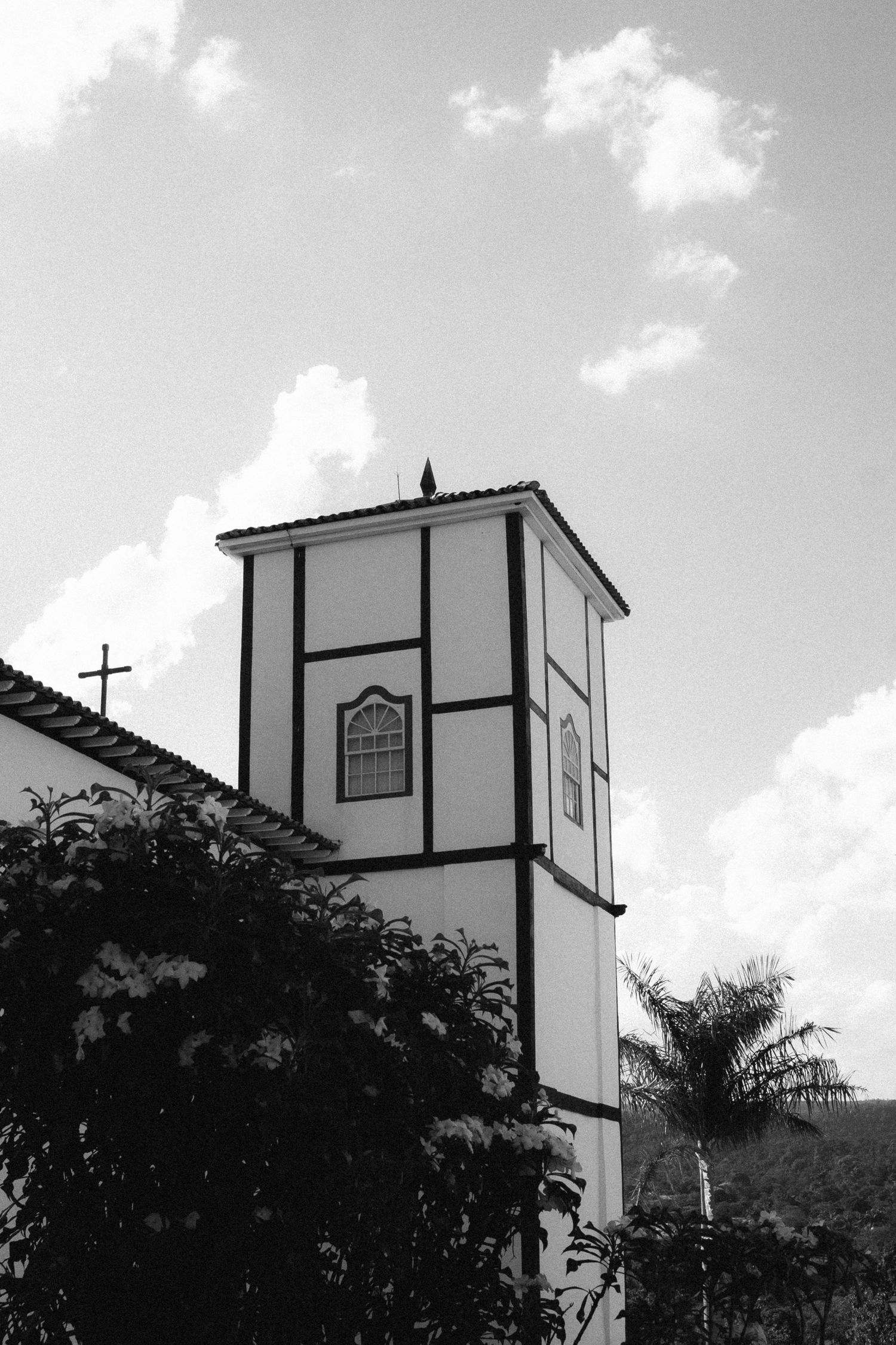 Black and white photo of historic church tower with cross and arched windows against cloudy sky.