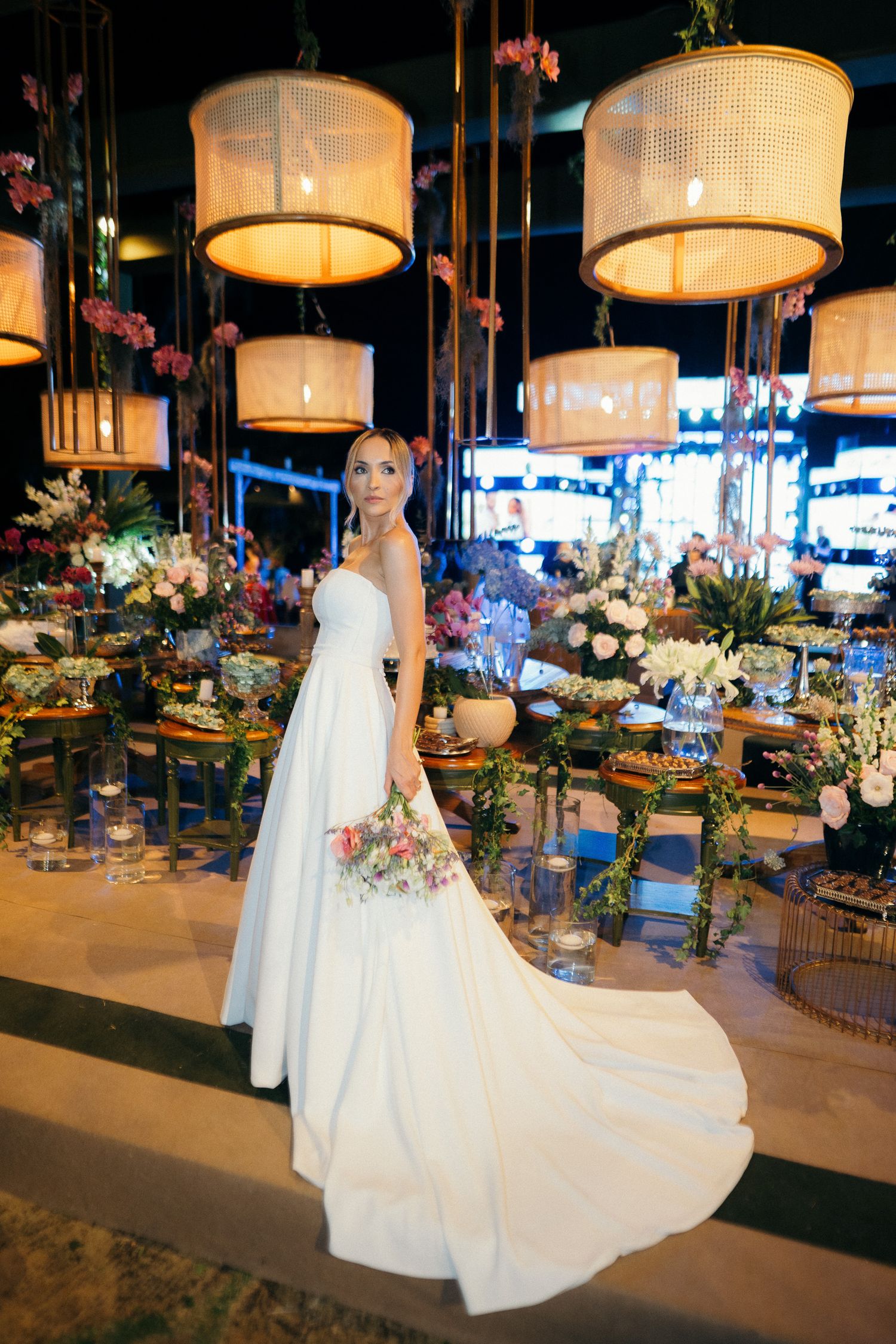 Bride in strapless ball gown with bouquet poses in elegantly decorated wedding reception hall.