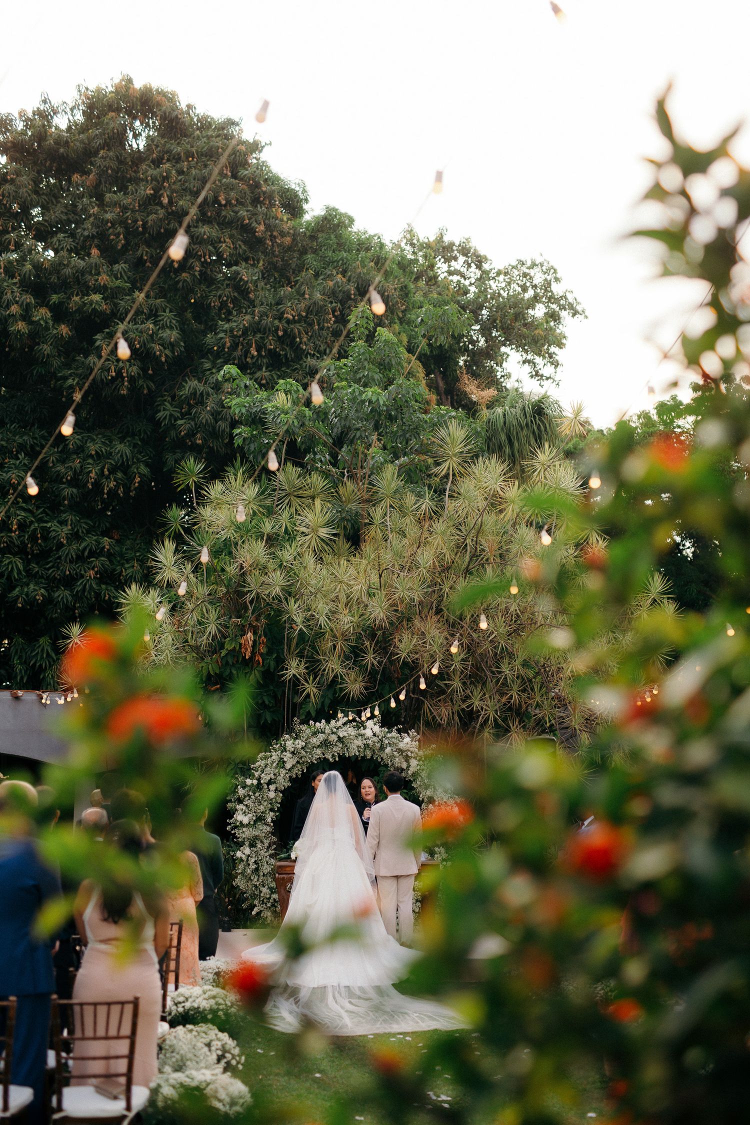 Romantic outdoor wedding ceremony under string lights with bride and groom at altar.