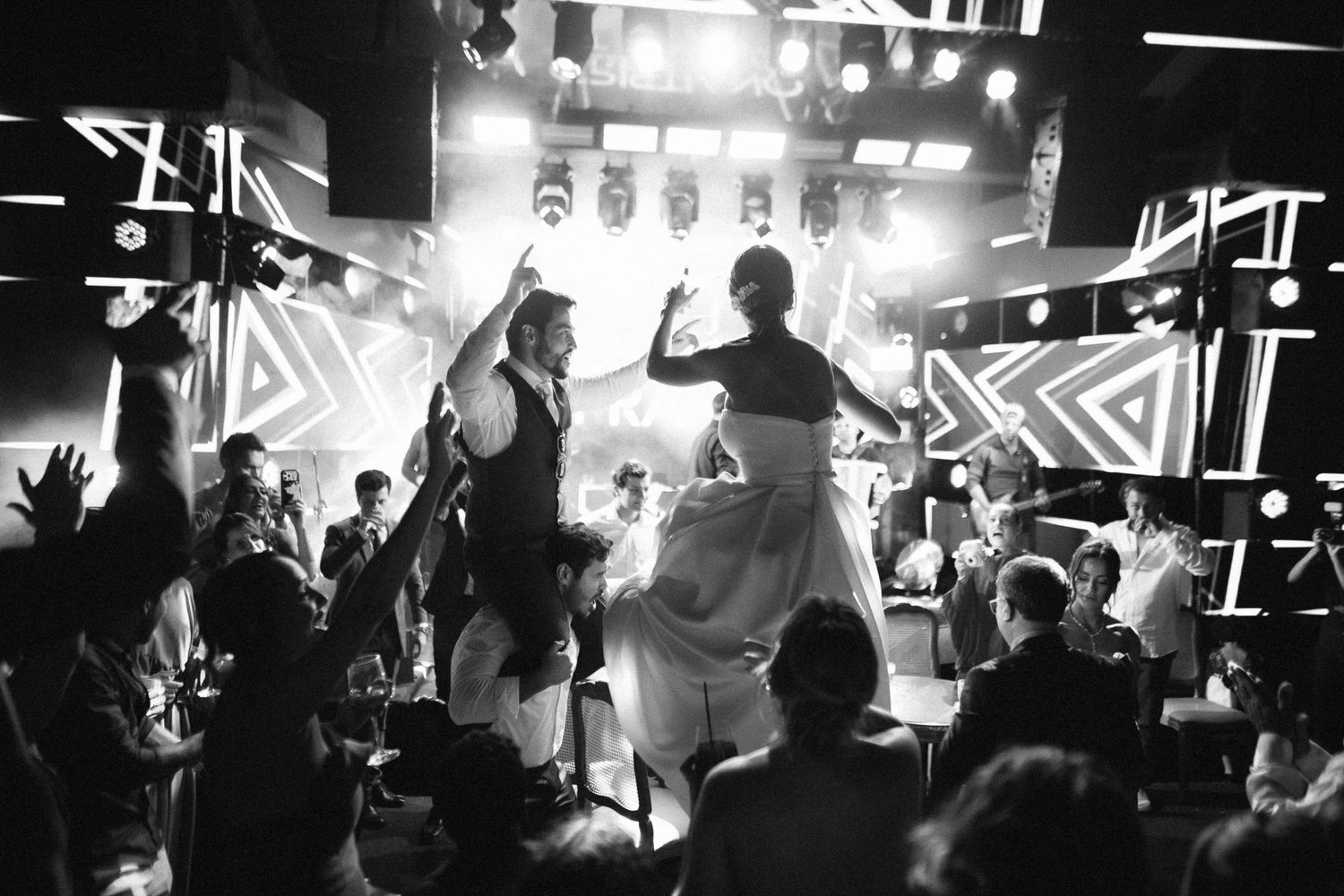 Black and white photo of bride and groom dancing on stage at lively wedding reception.