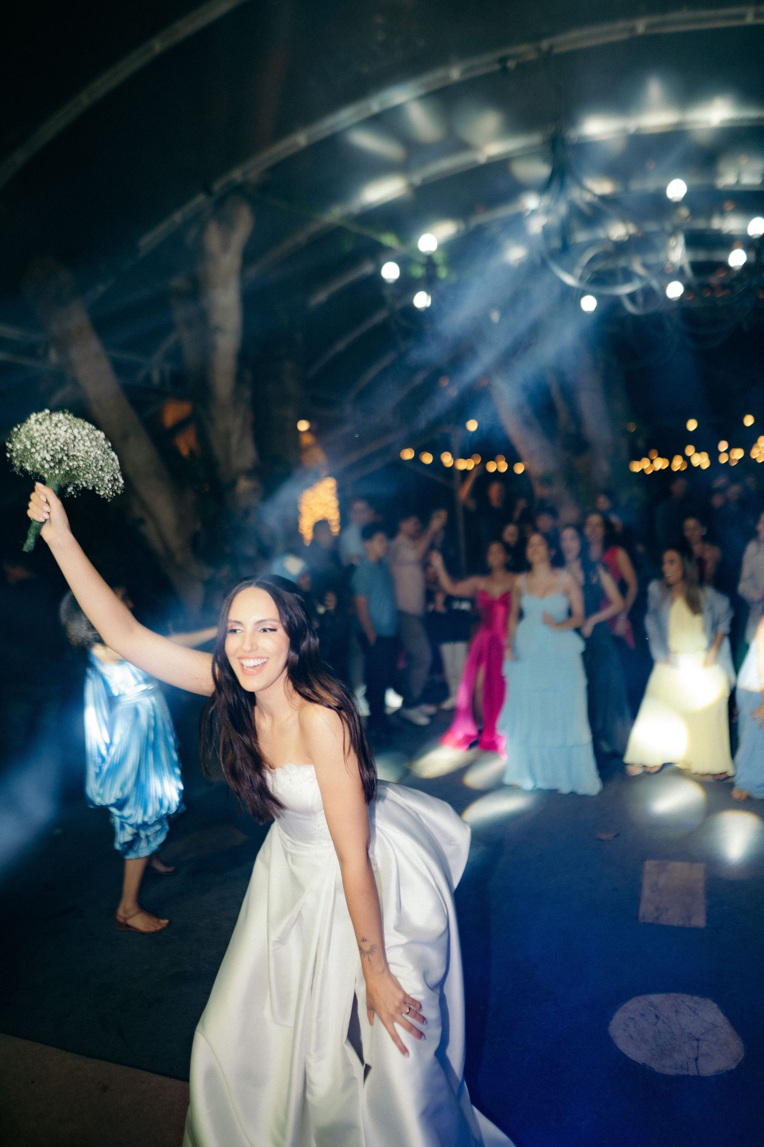 Bride triumphantly raises bouquet before tossing it to guests at festive wedding reception.