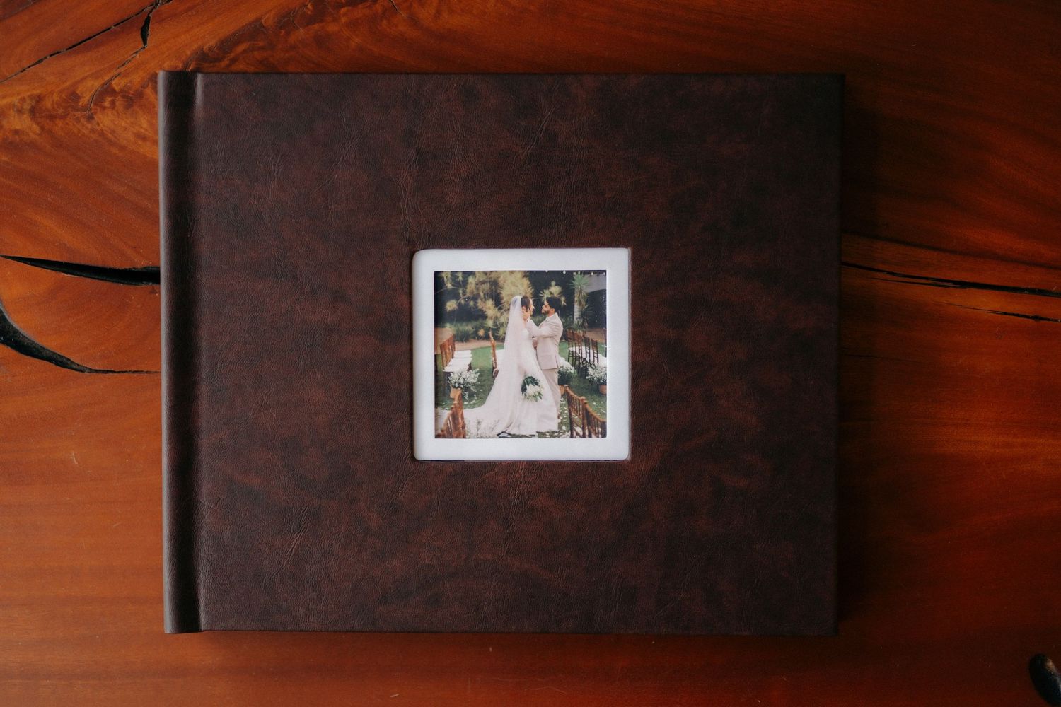 Dark brown leather wedding photo album with a polaroid-style cover photo of two brides on a wooden surface.