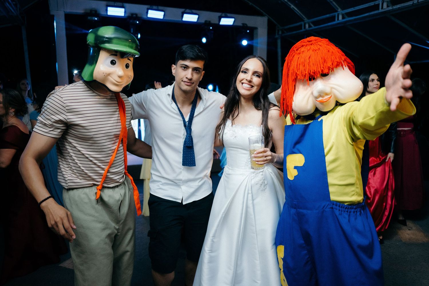 Bride and groom posing happily with colorful cartoon mascot characters at their fun wedding reception.