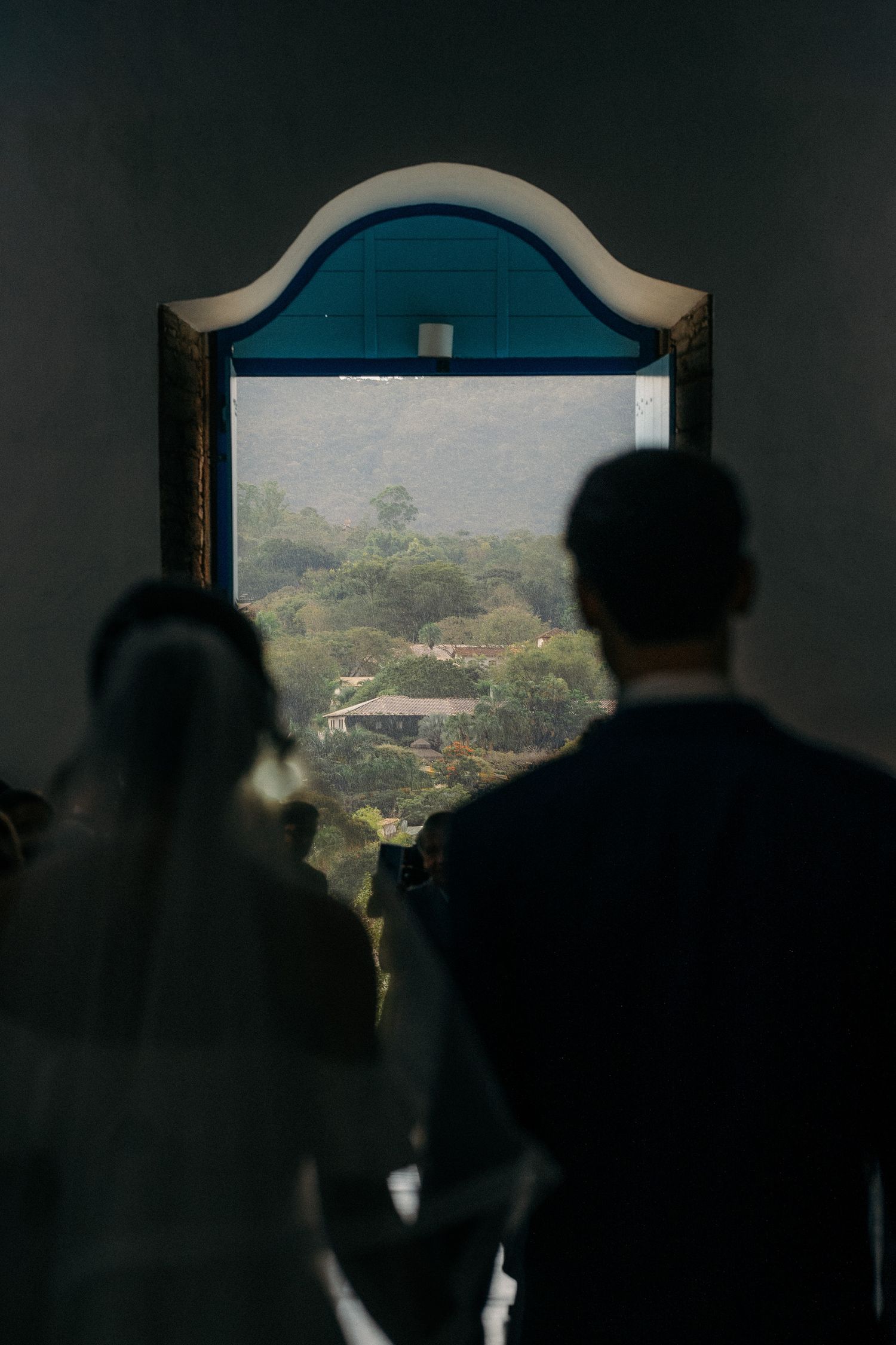 Silhouettes of bride and groom looking through an arched window at a scenic misty landscape during their wedding day.