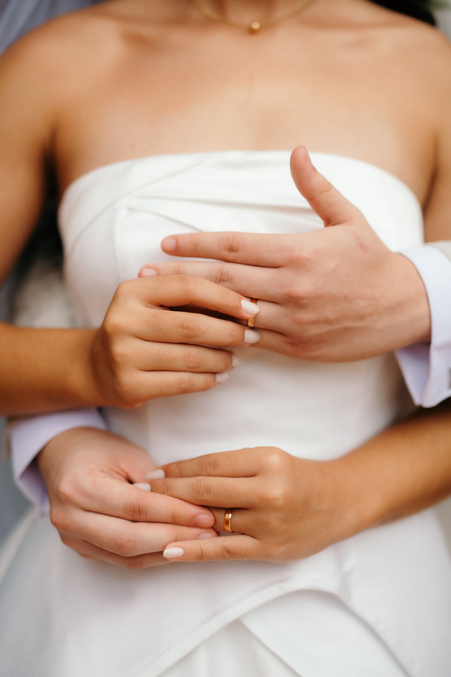 Close-up of bride and groom hands showing gold wedding rings against a white bridal gown.