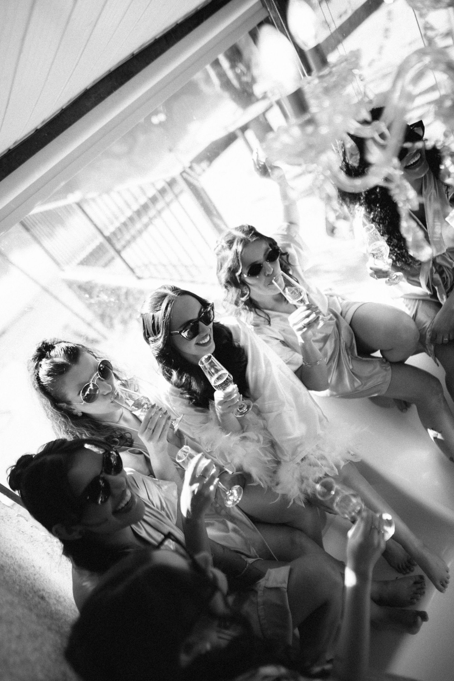 Bridesmaids in robes celebrating bachelorette party with champagne and sunglasses in black and white.