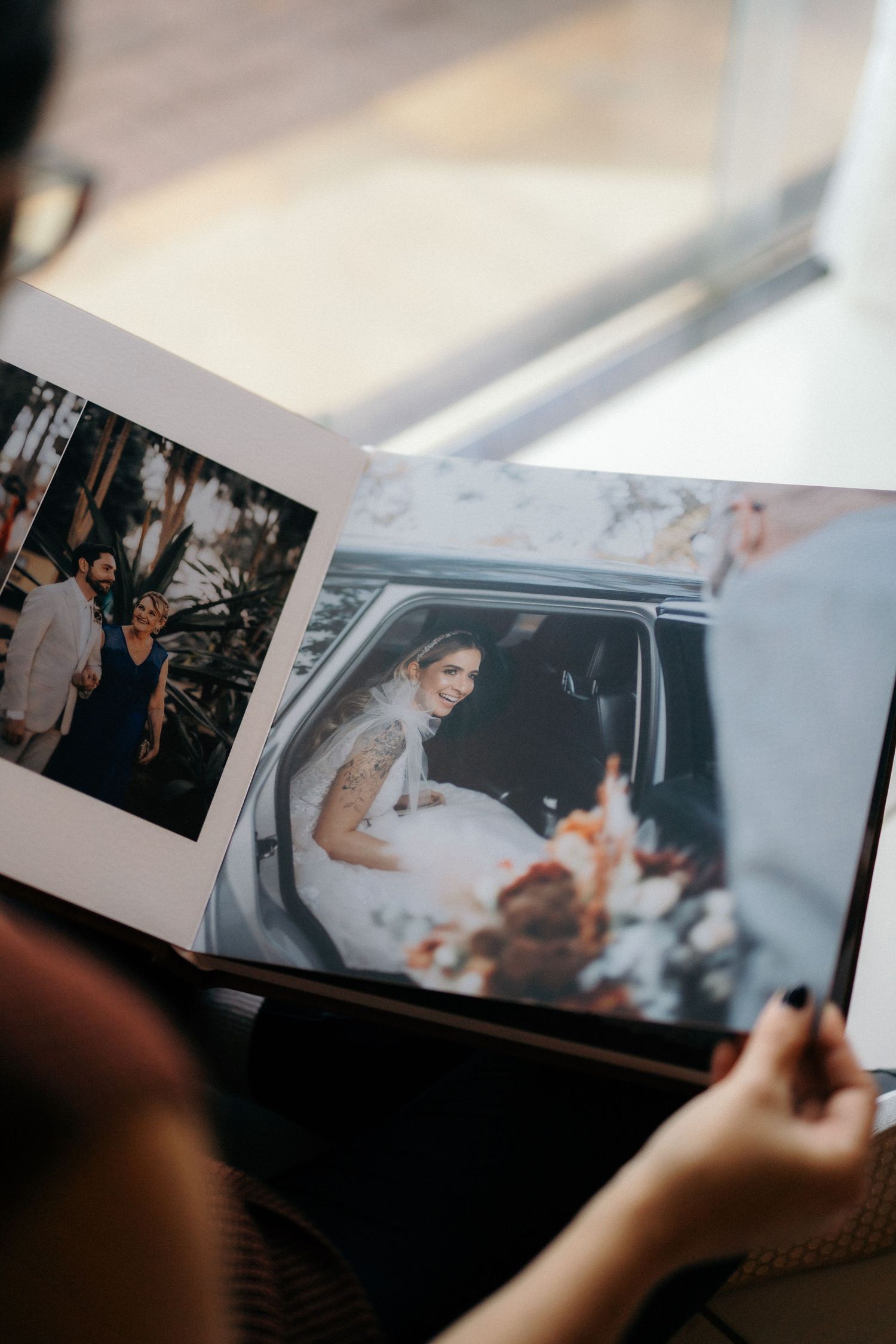 Person holding open a wedding photo album showing a bride in a car and group photos from the ceremony.