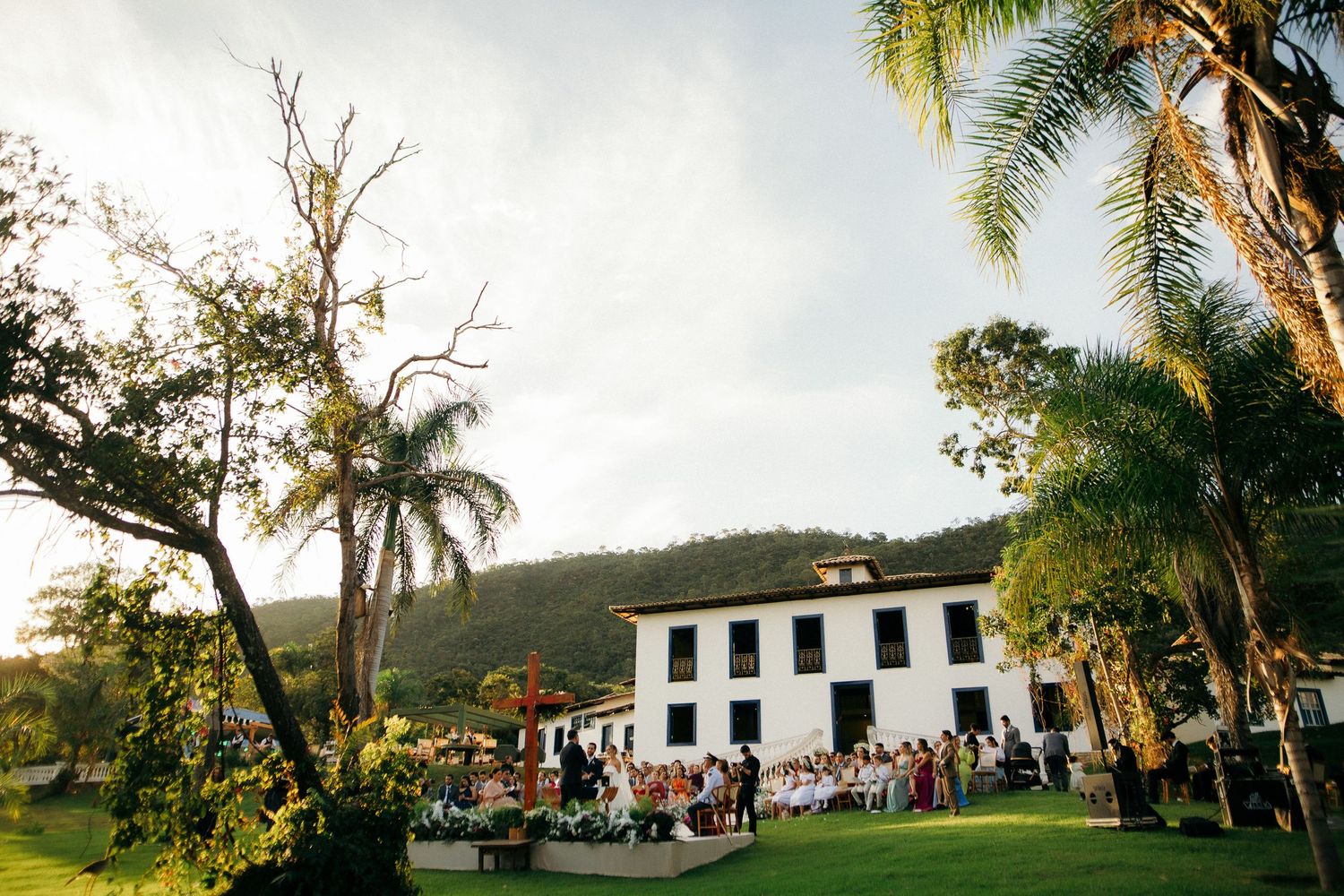 Outdoor wedding ceremony at historic white colonial estate surrounded by palm trees and mountains.