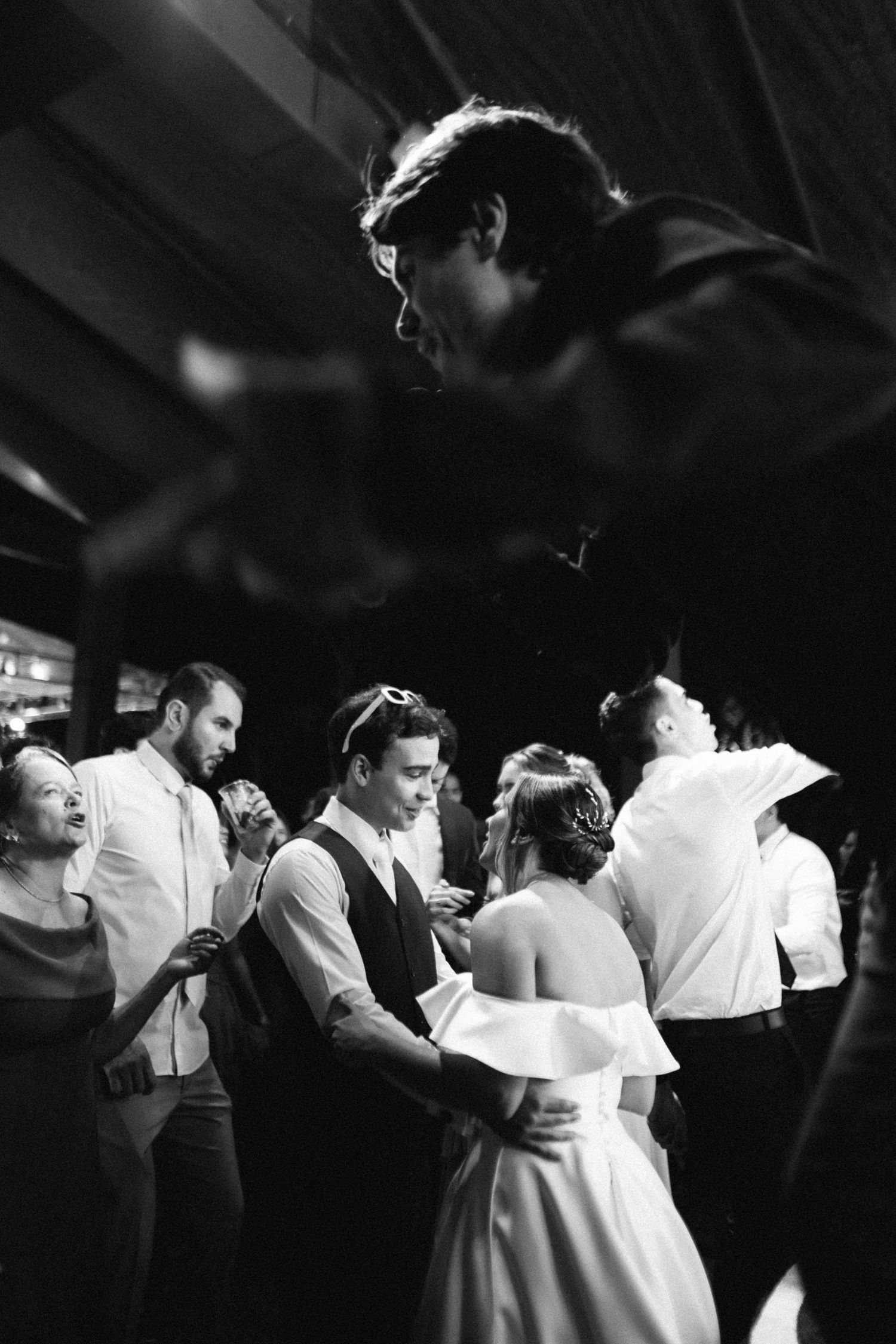 Black and white photo of bride and groom sharing a dance surrounded by guests at a wedding reception.