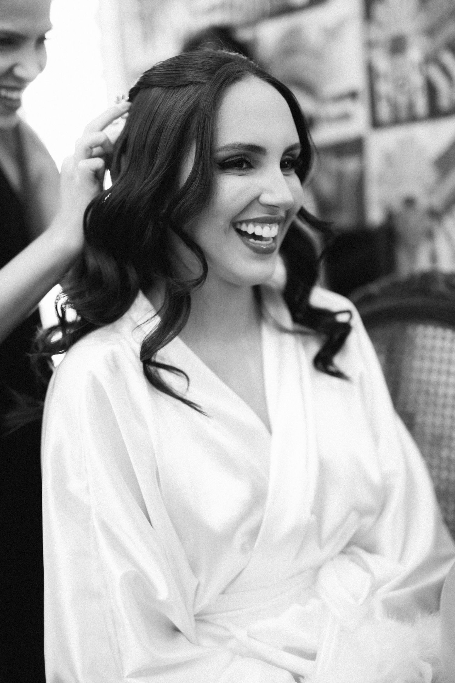 Black and white photo of a radiant bride laughing joyfully while getting her hair styled before her wedding.
