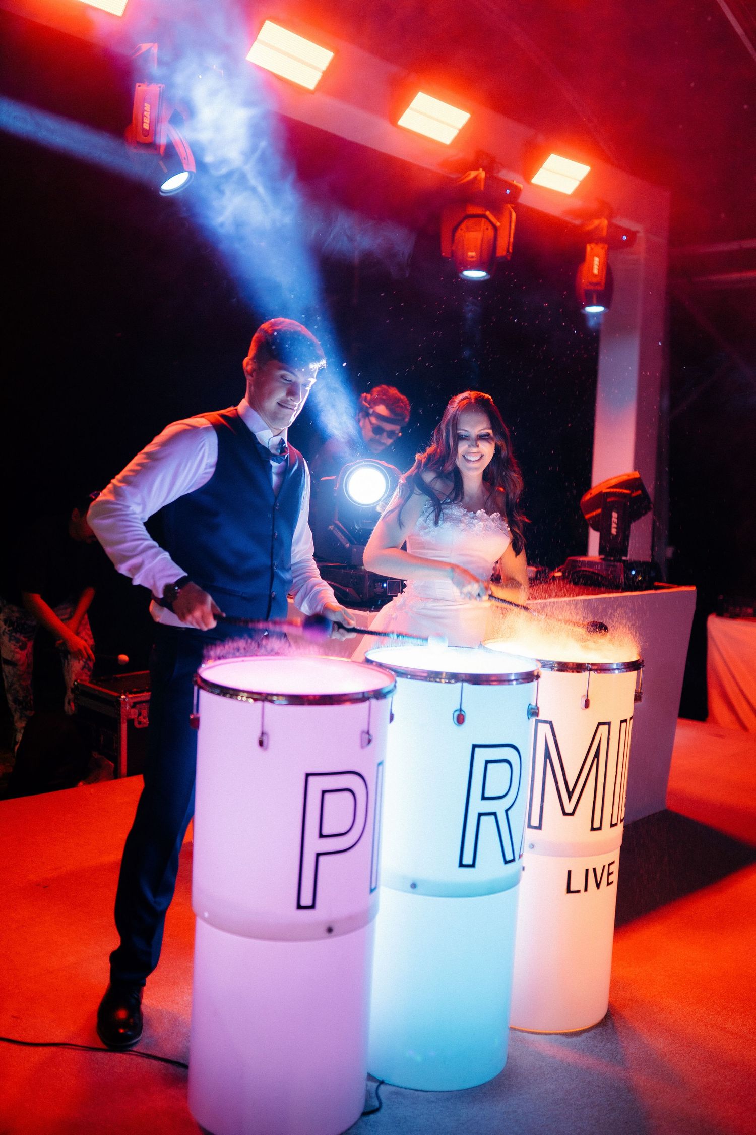 Bride and groom perform dramatic drum show with smoke effects under colorful stage lights at reception.