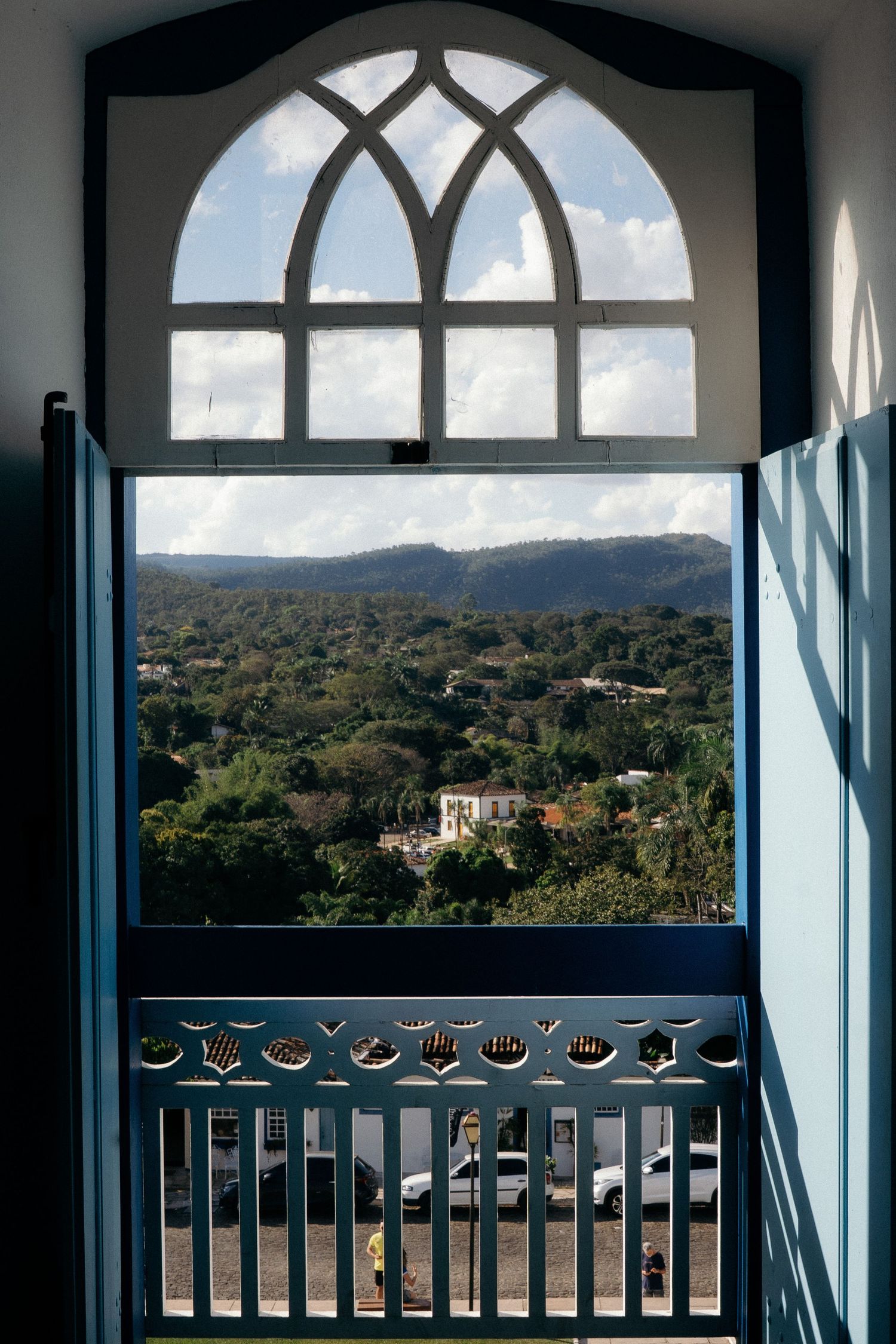 View through an arched blue church door overlooking lush green hills and tropical landscape.
