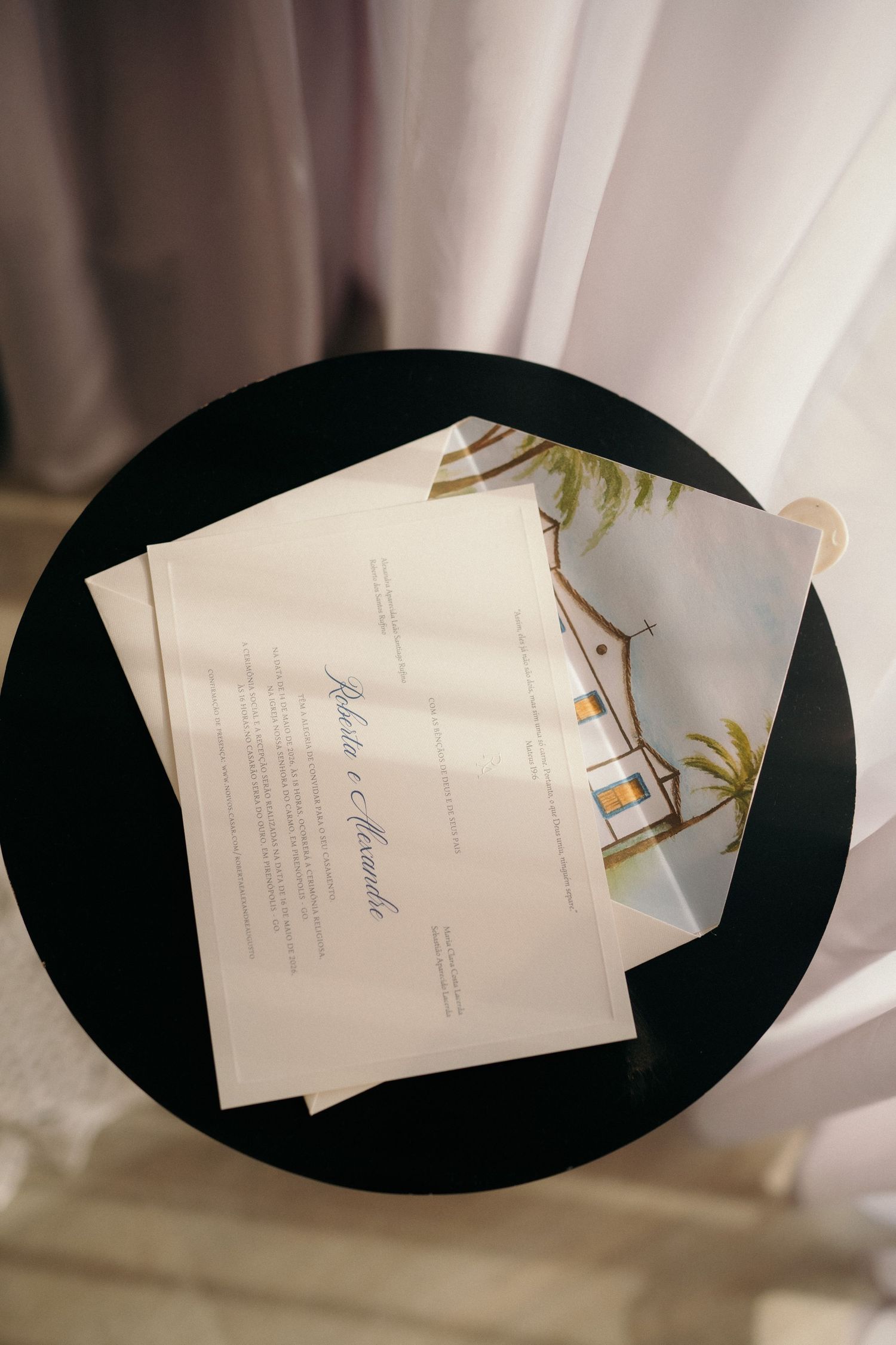 Elegant wedding invitation suite with illustrated venue card on a black round table with soft curtain backdrop.