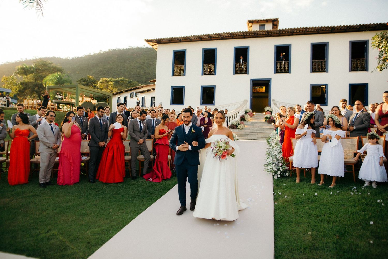Bride and groom walk down aisle at outdoor wedding ceremony at historic white estate.