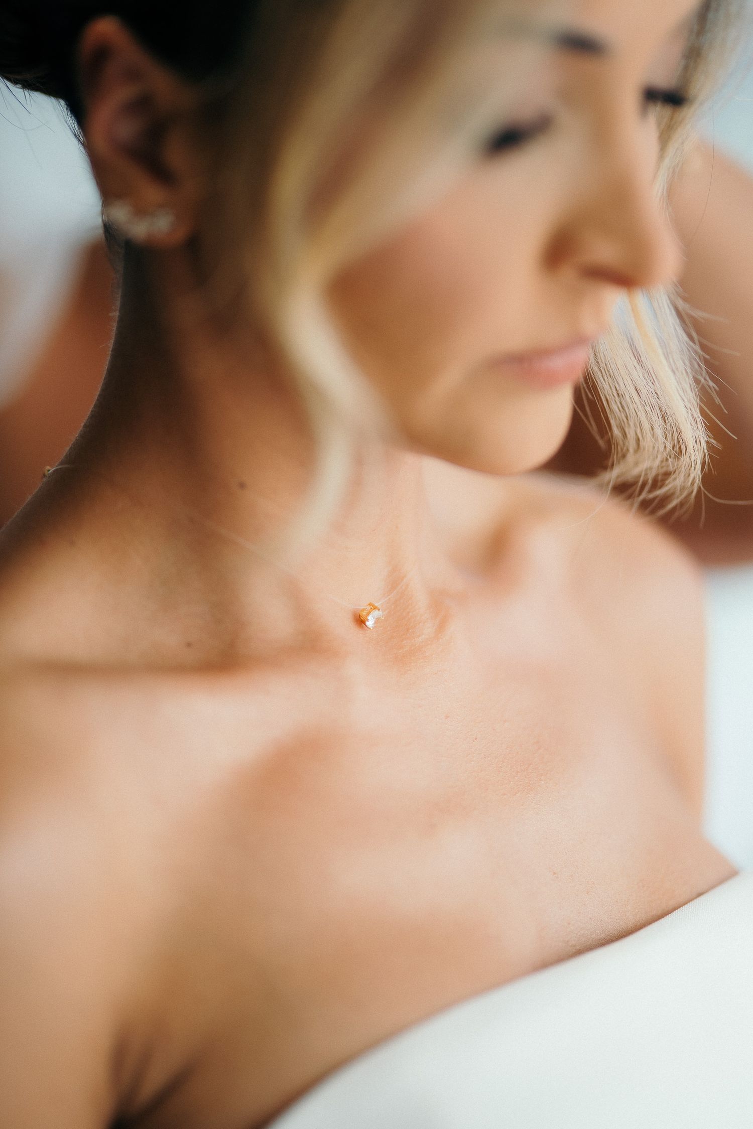 Close-up of a bride wearing a delicate pearl necklace and earring with soft natural lighting highlighting her collarbone.