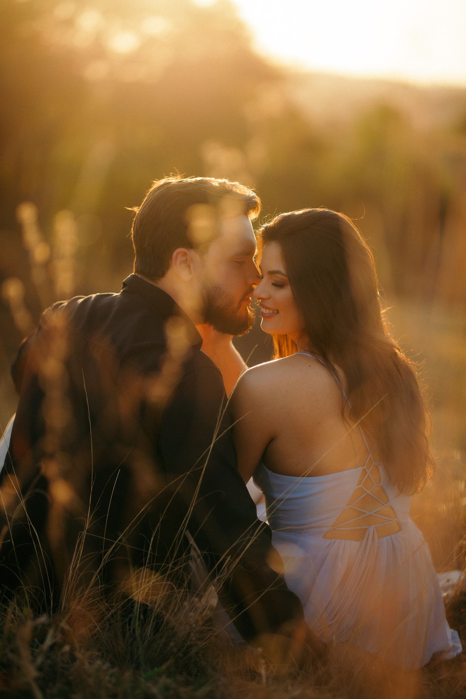 Couple nearly kissing in warm golden sunset light in an open field.
