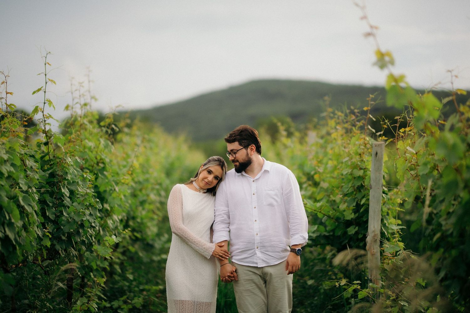Couple embracing tenderly in a lush green vineyard with hills behind.