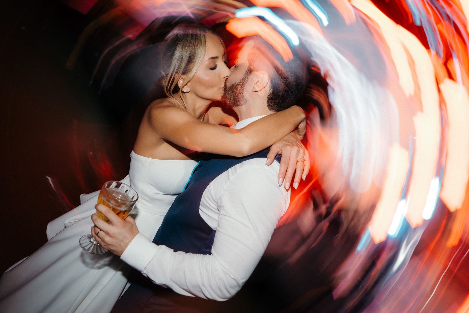 Newlyweds share a romantic embrace surrounded by swirling colorful bokeh lights.