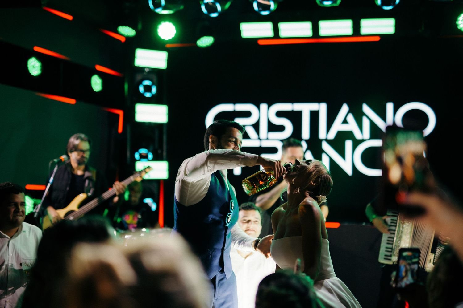 Trumpet player performs energetically for crowd at wedding reception with Cristiano Neto band on illuminated stage.