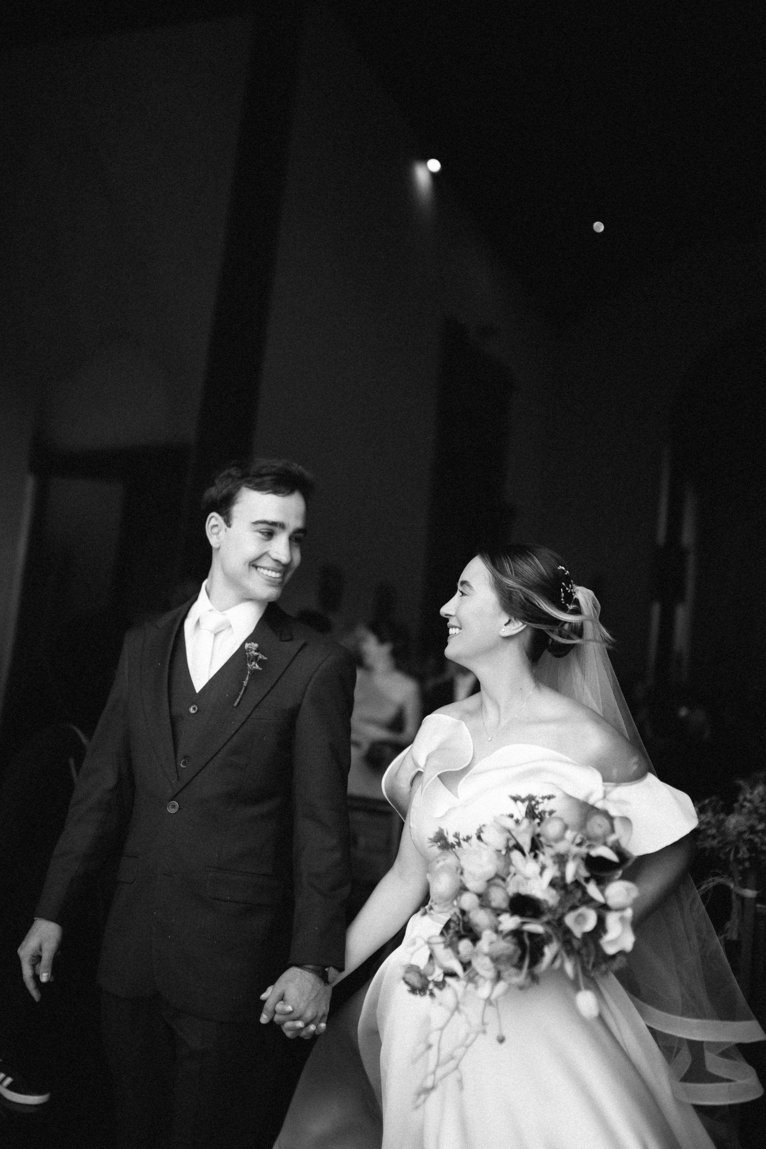 Black and white photo of smiling newlyweds holding hands walking down the aisle after their wedding ceremony.
