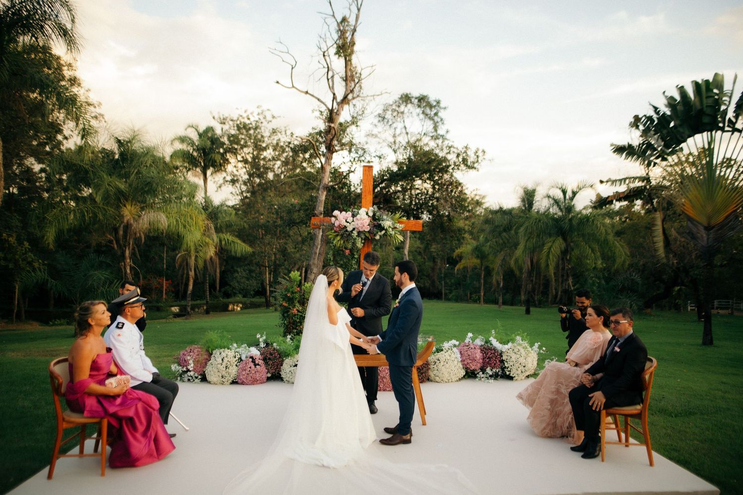 Bride and groom stand at the altar beneath a wooden cross at an outdoor wedding.