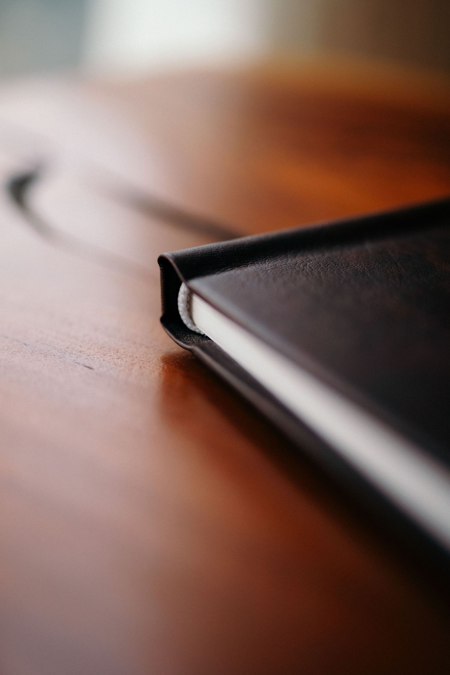 Close-up of a black leather-bound notebook resting on a wooden table with shallow depth of field.