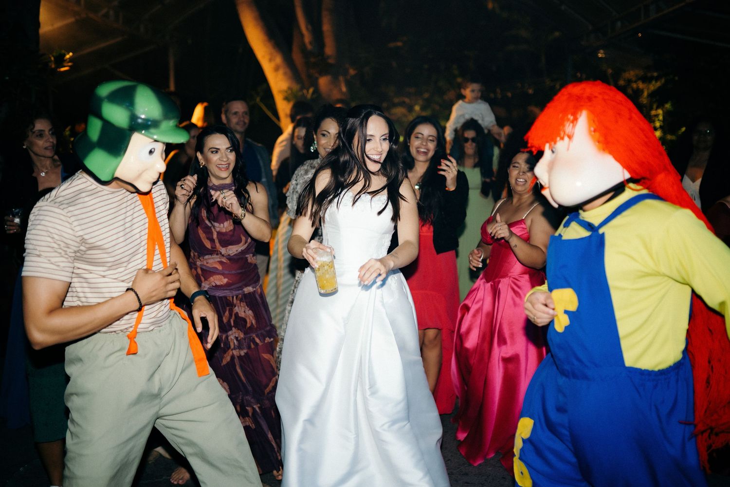 Bride dances with costumed guests including Mario characters at fun outdoor wedding reception.