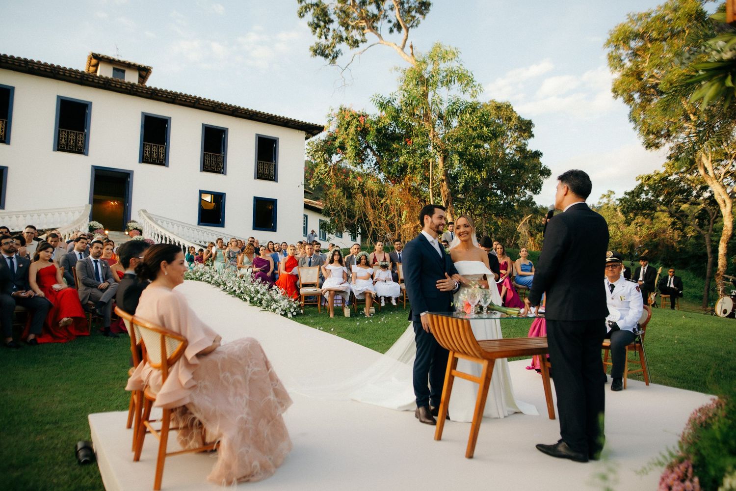 Couple exchanges vows at an outdoor wedding ceremony on a lush green lawn.