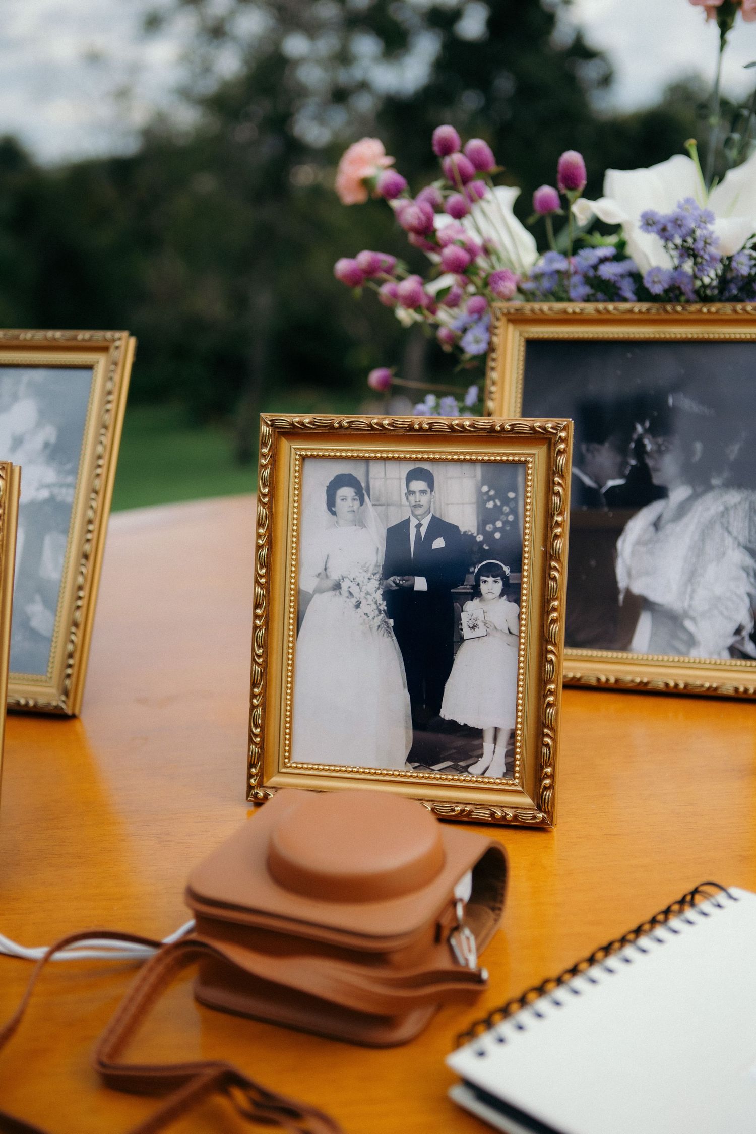 Vintage gold-framed black and white wedding photos displayed on wooden table with flowers and guest book.